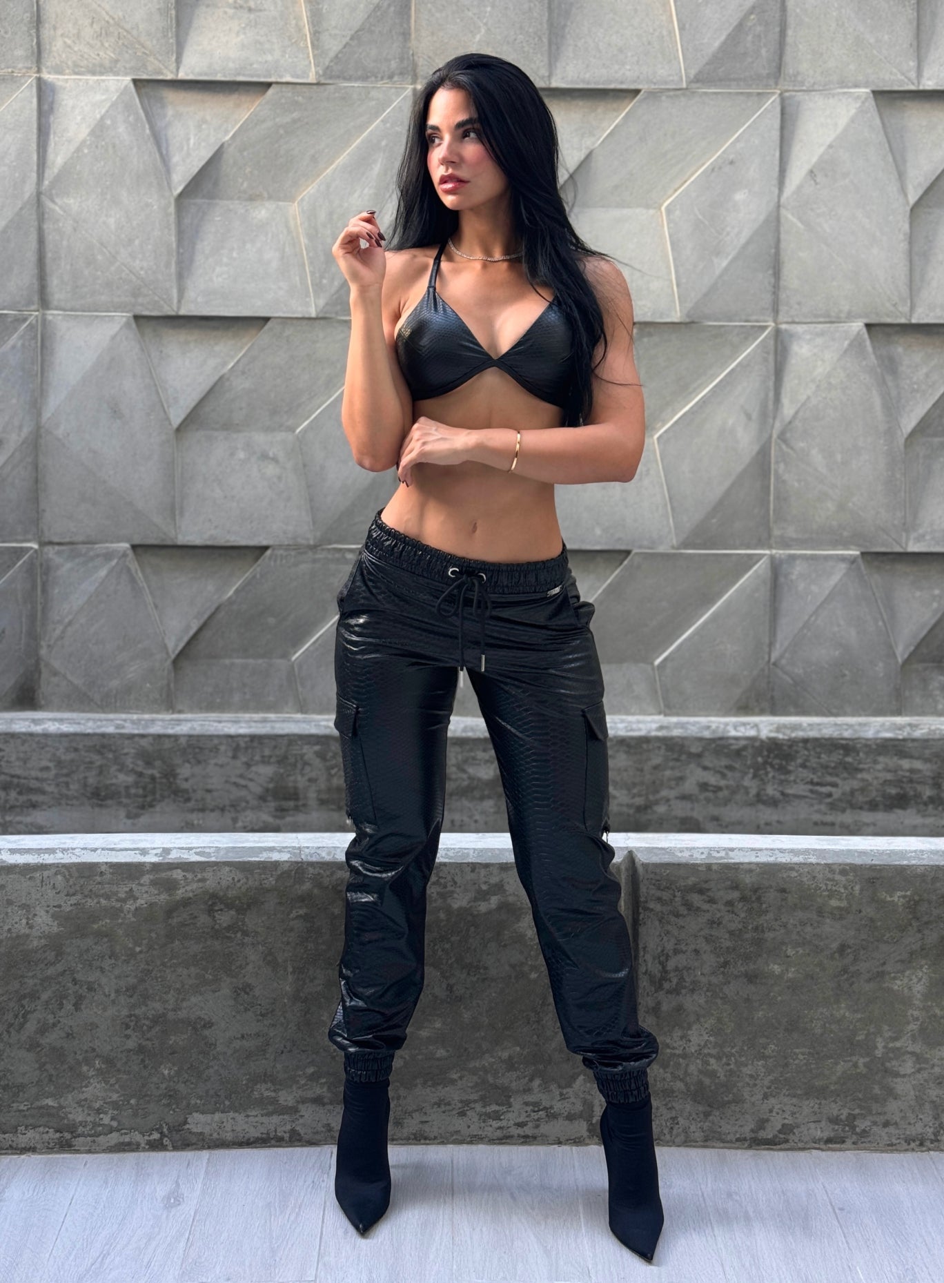 Woman wearing a black snake-embossed bralette and matching cargo joggers with drawstring waist, paired with black pointed-toe boots.