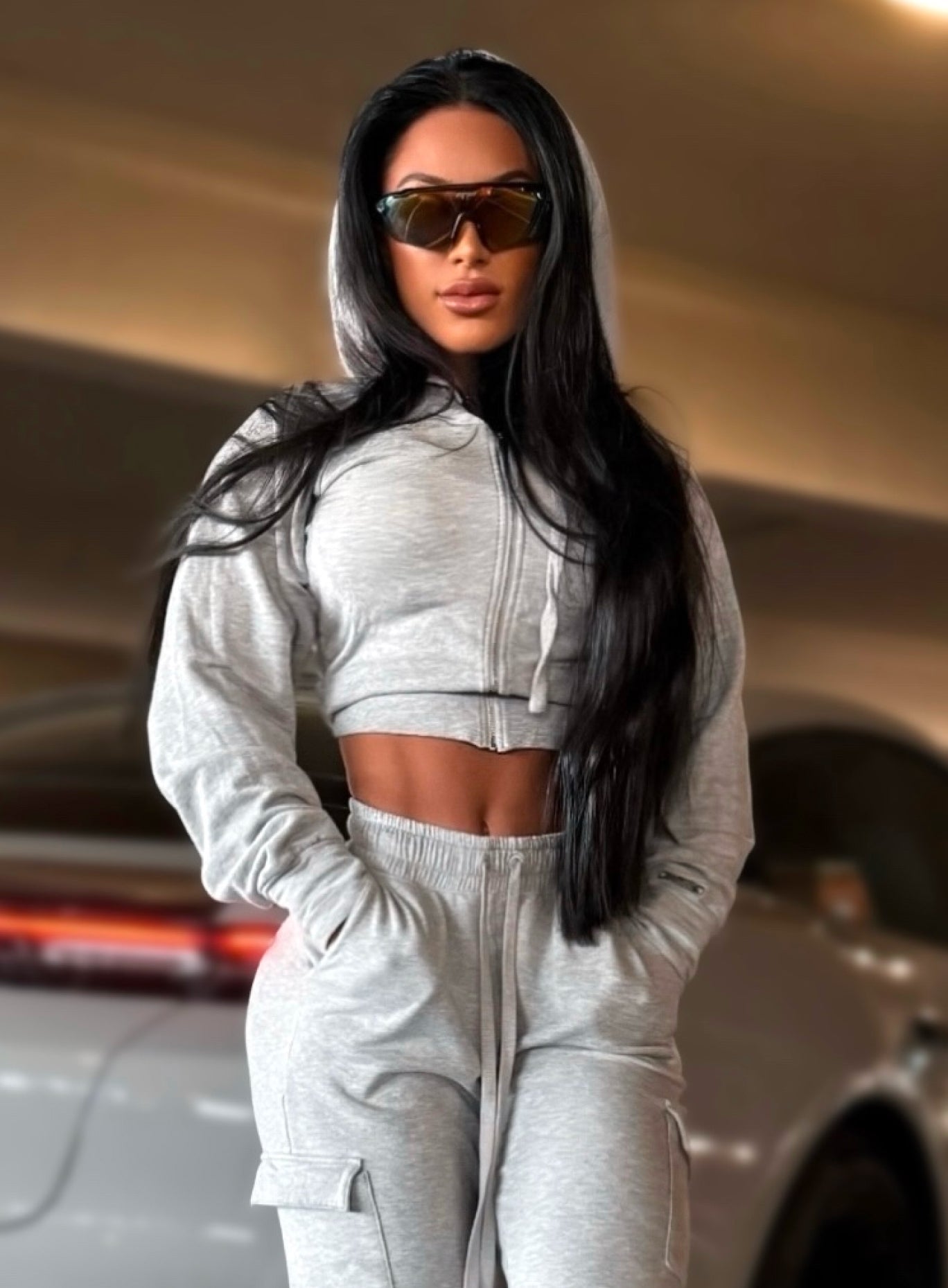 Woman wearing a light heather gray cropped zip-up hoodie and matching cargo joggers, styled with oversized sunglasses.
