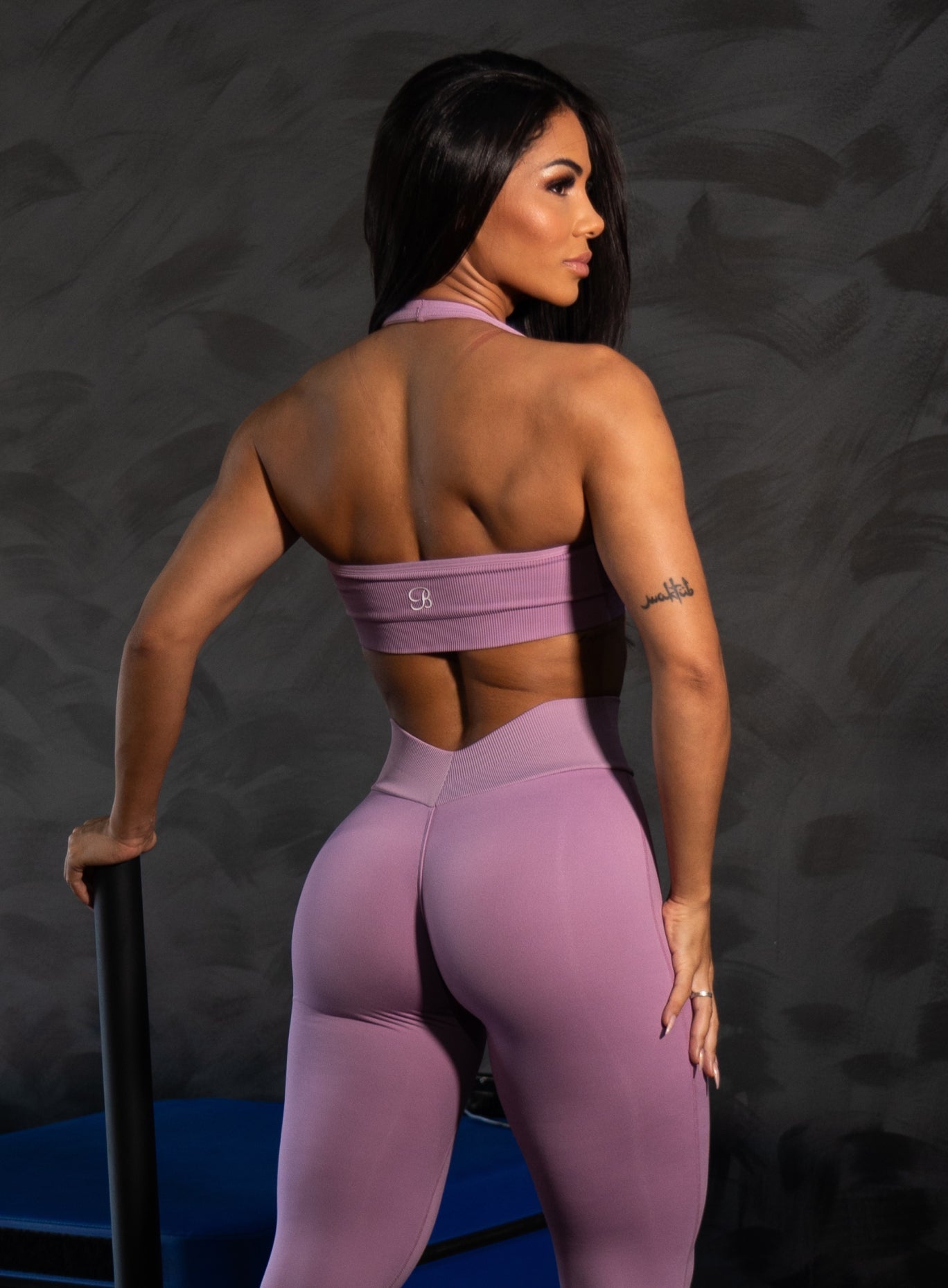Back view of a woman wearing a purple seamless sports bra and matching high-waisted v-back leggings with a sculpting fit.