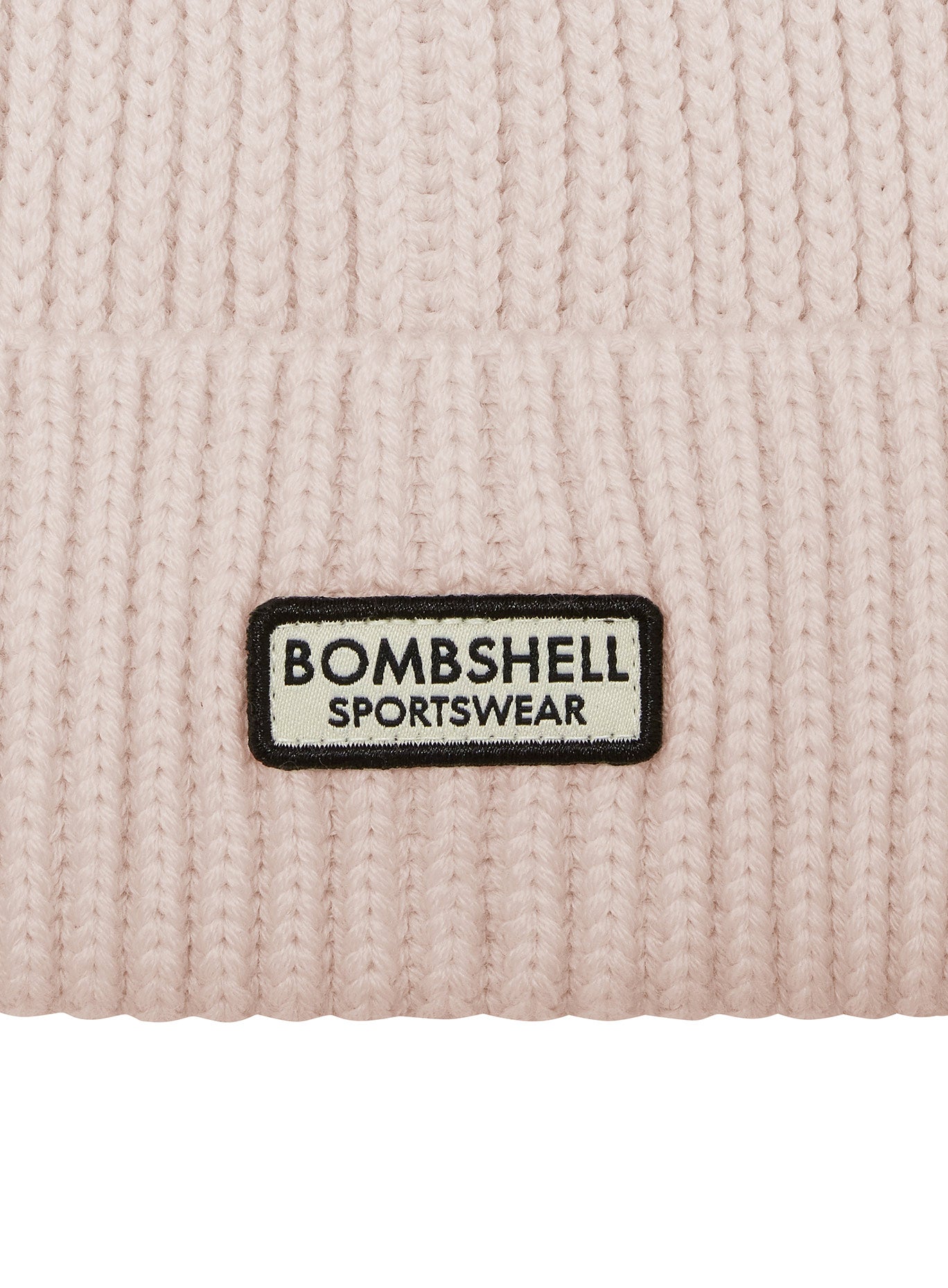 Close-up of the silver Bombshell Sportswear logo on the cream B Beanie, a cozy knit winter hat.