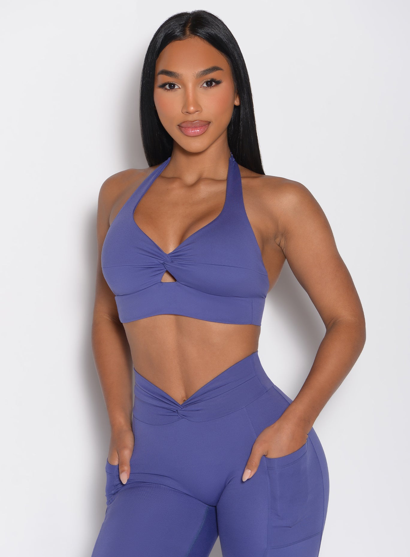 front profile view of a model with both hands inside the side pockets wearing the Backless Knot Bra in future dusk color paired with the matching leggings