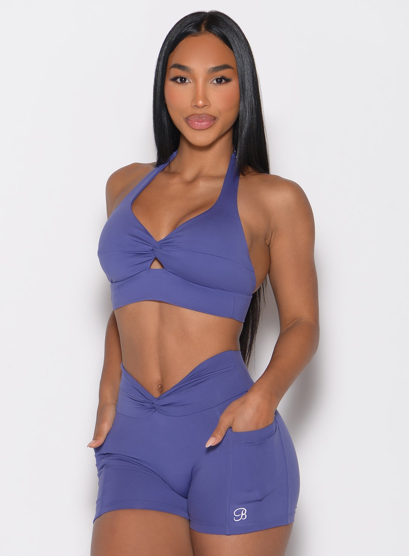 front profile view of a model with both hands inside the side pockets wearing the Backless Knot Bra in future dusk color paired with the matching shorts