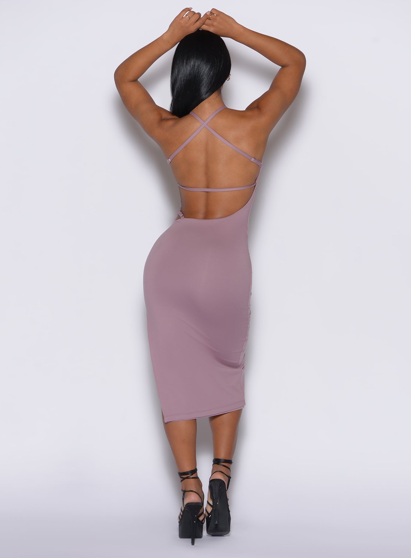 back profile view of a model with her hands over her head wearing our bombshell bunny dress in light mauve color