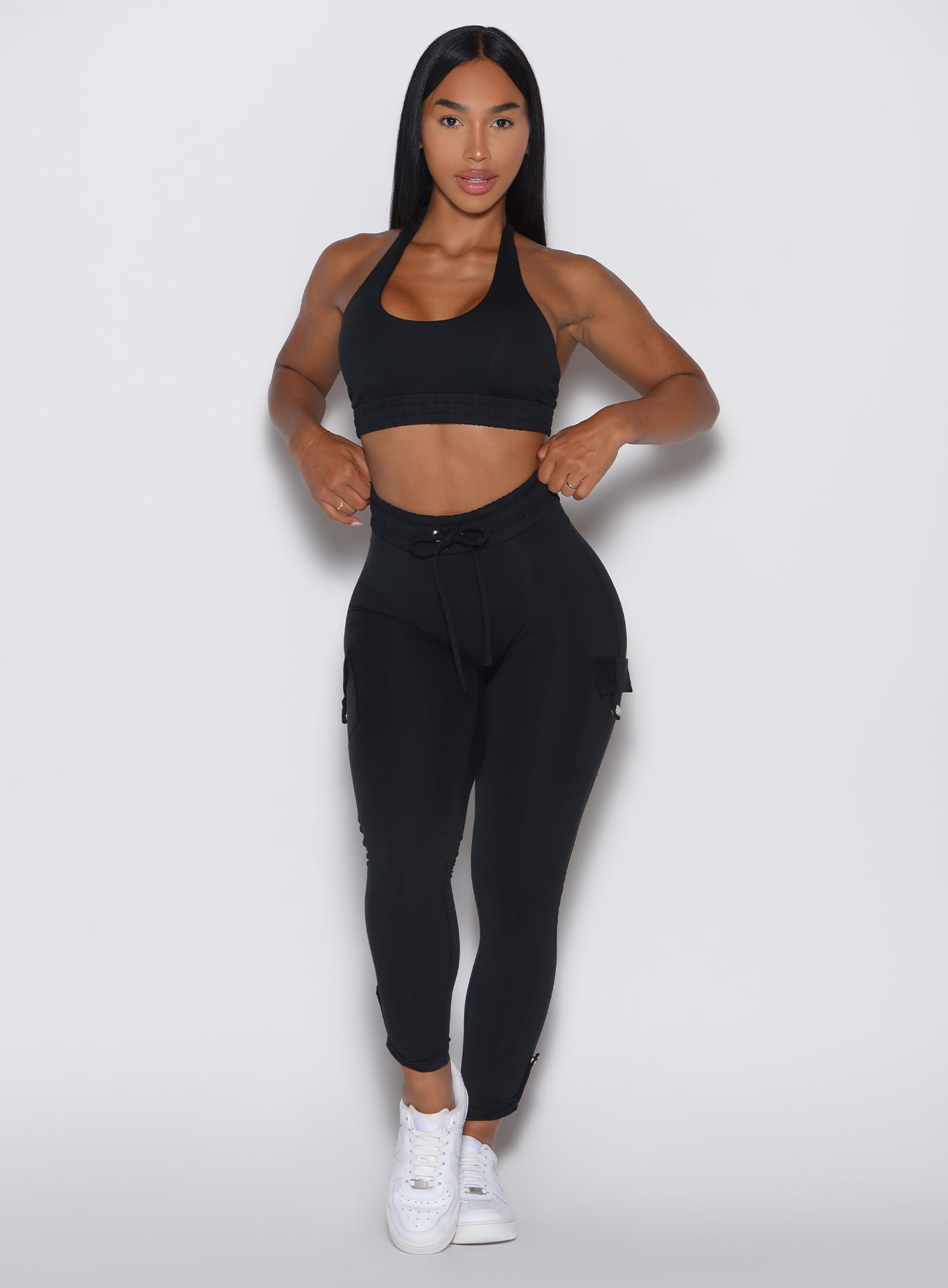 front profile view of a model adjusting the waistband wearing the Cargo Edge Leggings in Black color