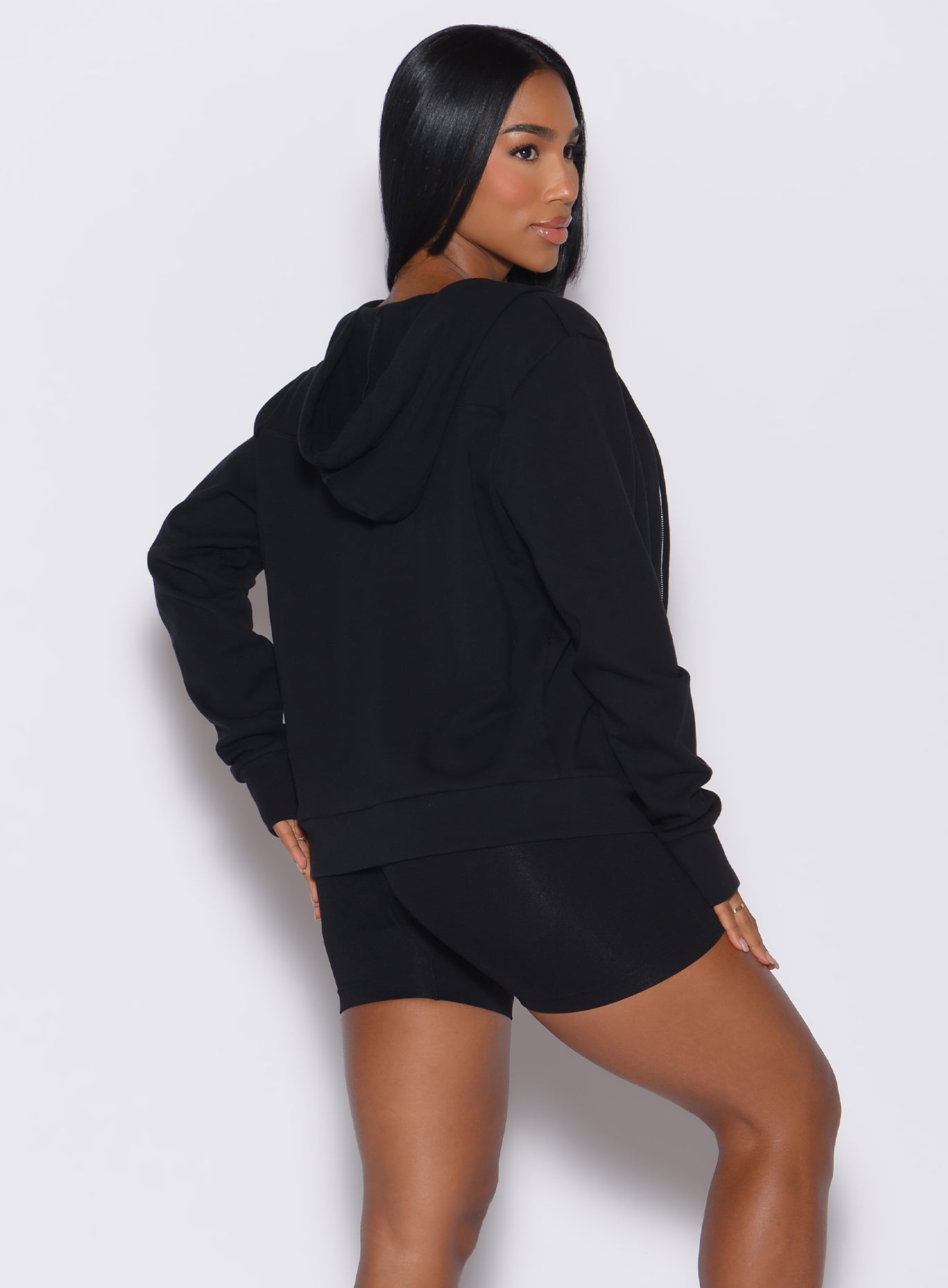 back profile view of a model facing to her right wearing our black oversized hoodie, along with matching shorts