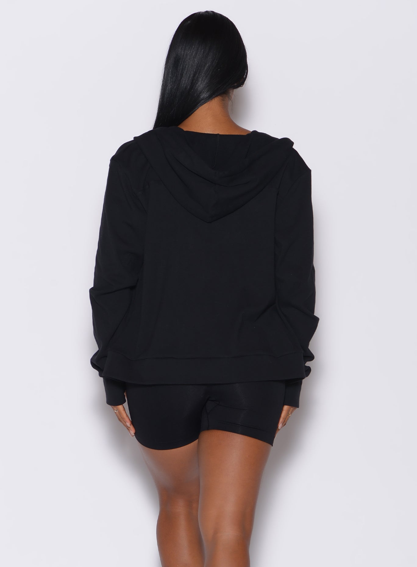 Back profile view of a model wearing our black oversized hoodie, along with matching shorts