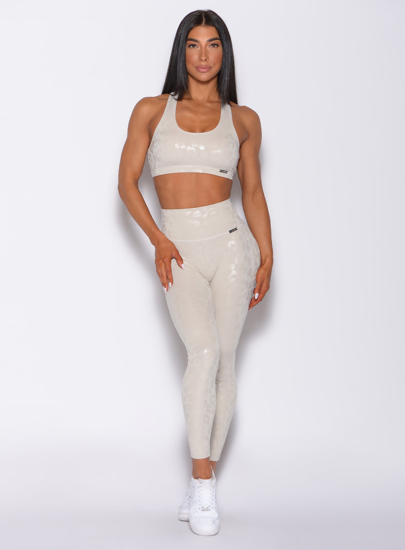 front profile picture of a model facing forward wearing our shine leopard leggings in buff leopard color along with a matching bra