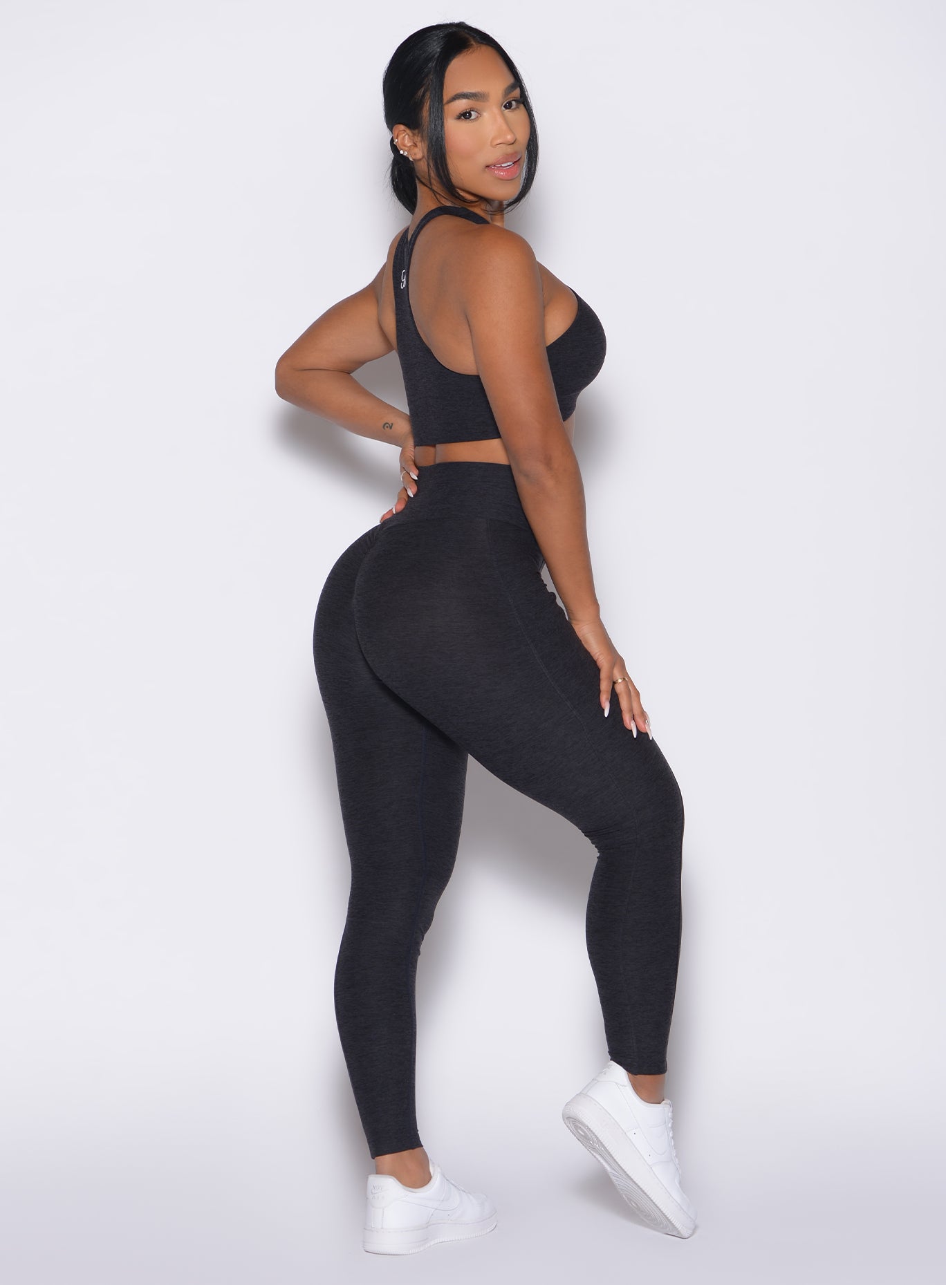 right side view of a model facing to her right wearing our Contour Leggings and the matching Cross Over Halter Bra in Heathered Black color