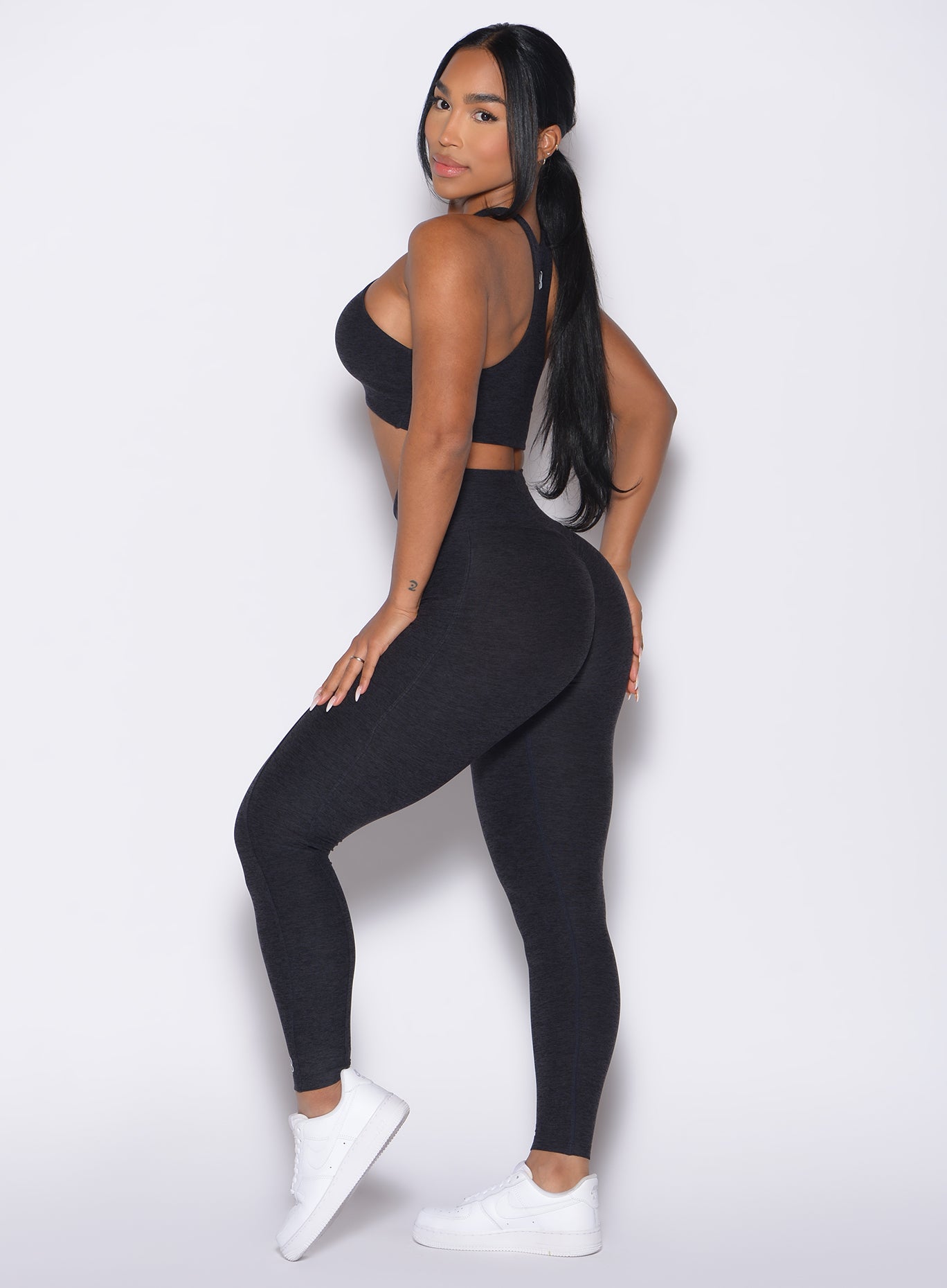 left side view of a model wearing our Contour Leggings and the matching Cross Over Halter Bra in Heathered Black color