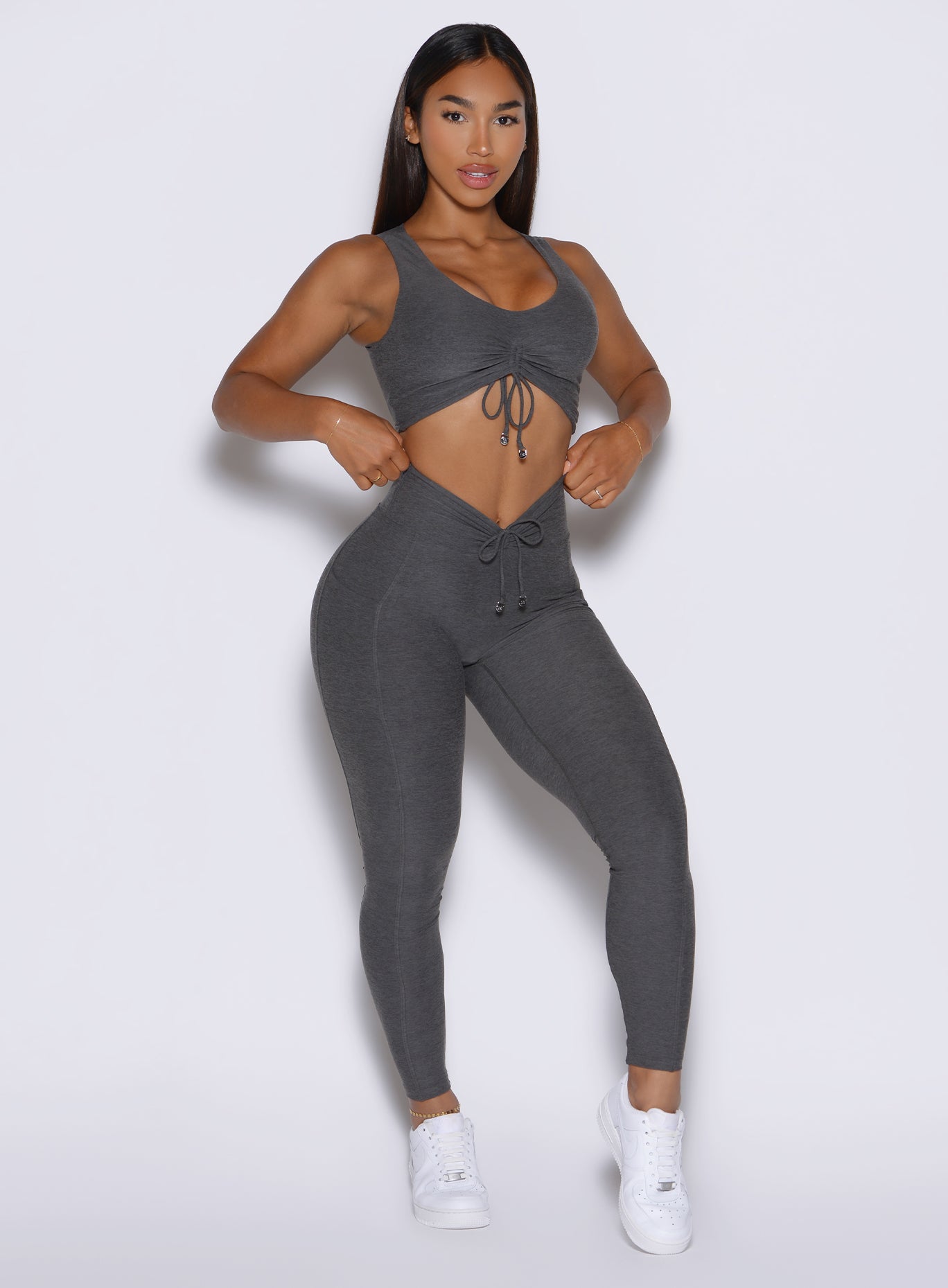 front profile view of a model holding the waistband of the leggings wearing the Charm Fit Leggings in Steel Shadow color