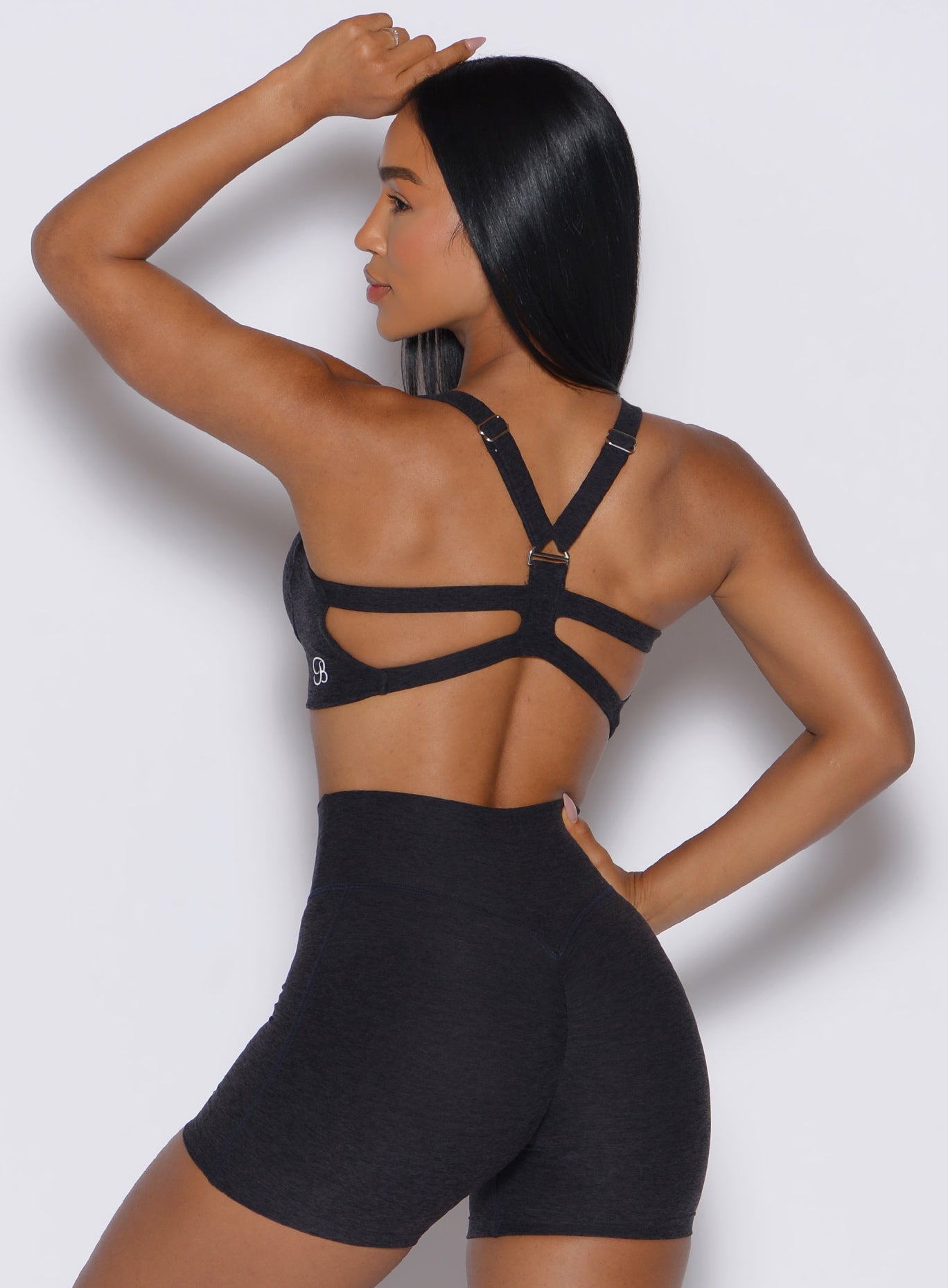 back view of a model wearing our core set bra with her hand over her head in heather black color along with the matching shorts
