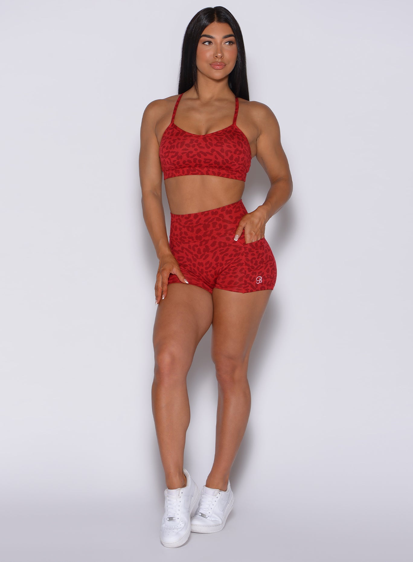 Front profile view of a model with her left hand in pocket wearing our curves shorts in red cheetah color along with a matching bra