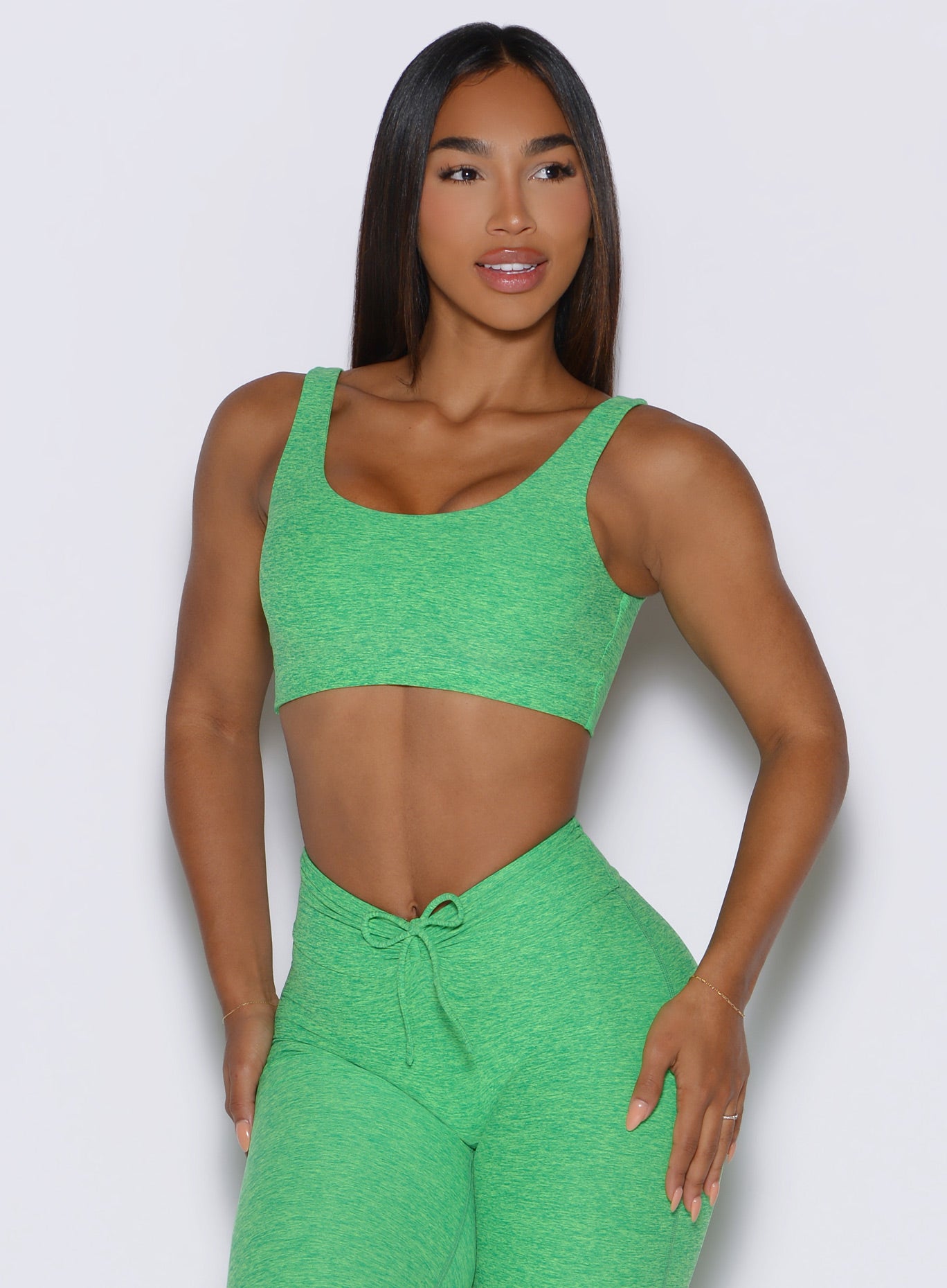 front left side profile view of a model holding the waistband of the shorts wearing the Dualmode Bra in neon miami beach color