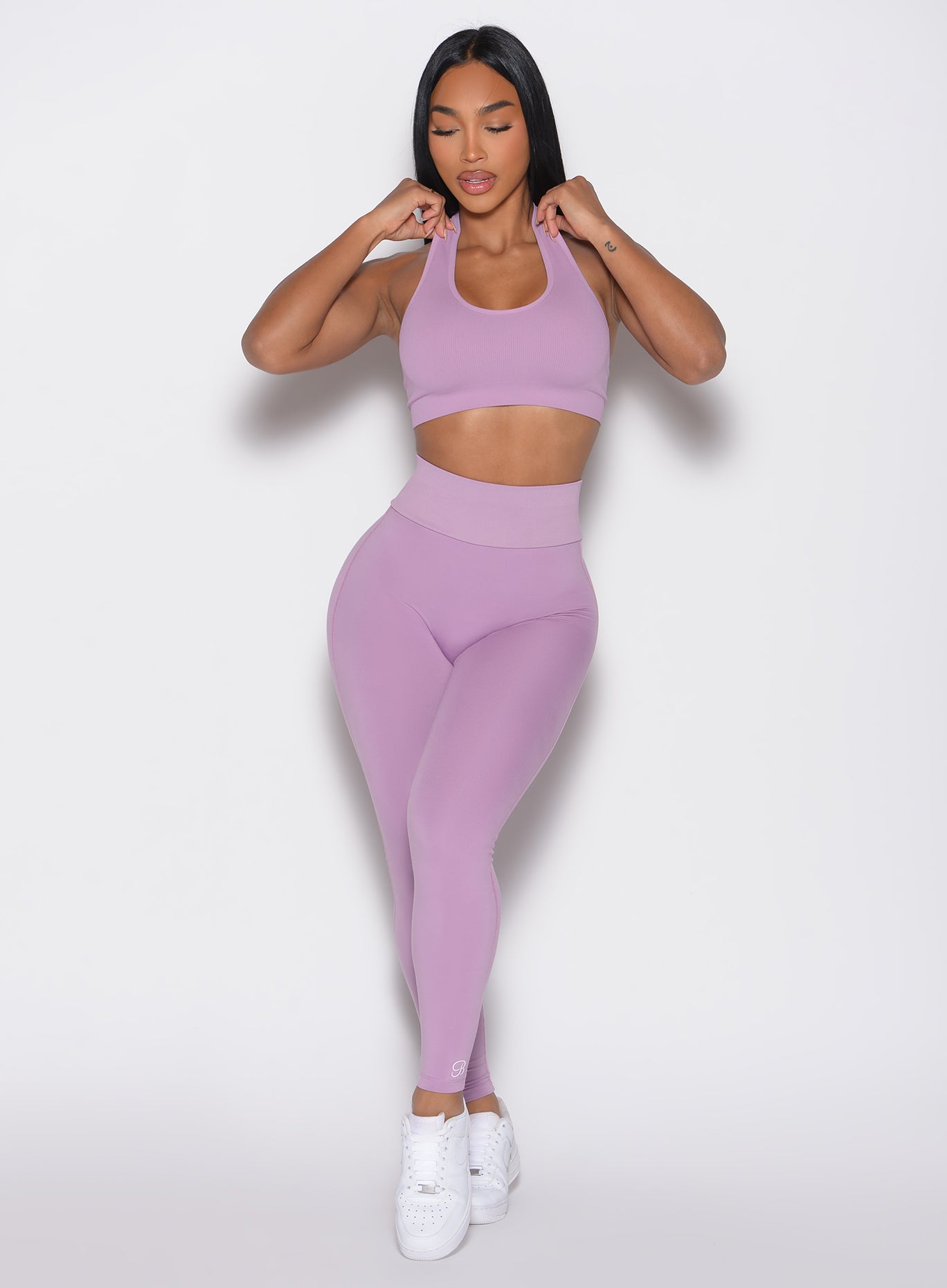 front profile view of a model with both hands on the straps of the top wearing the Figure Butt Lift Leggings in smokey grape color