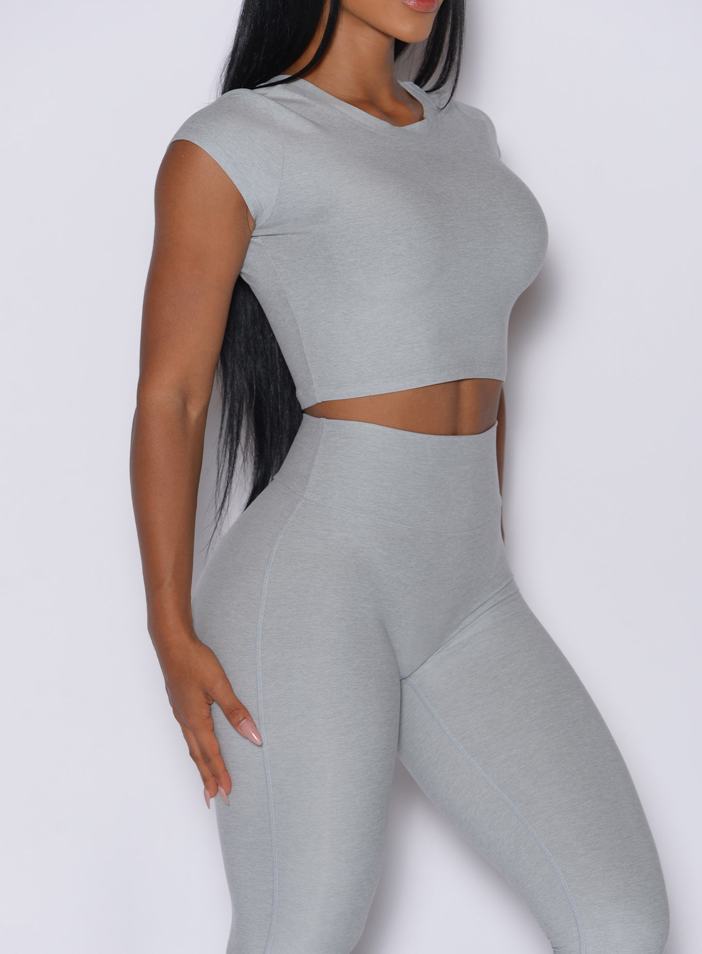 right side profile view of a model facing forward wearing our fit fam active tee in light cloud color along with the matching leggings