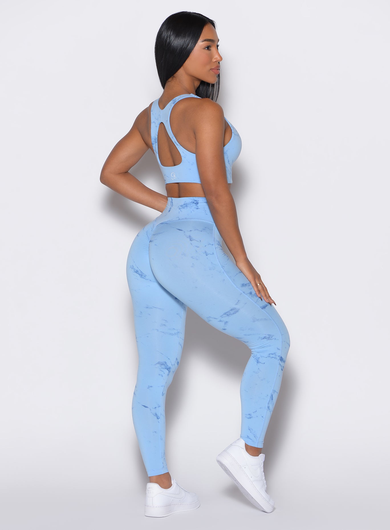 right side profile view of a model angled slightly to her left wearing our fit marble leggings in Blue Jay color along with a matching bra