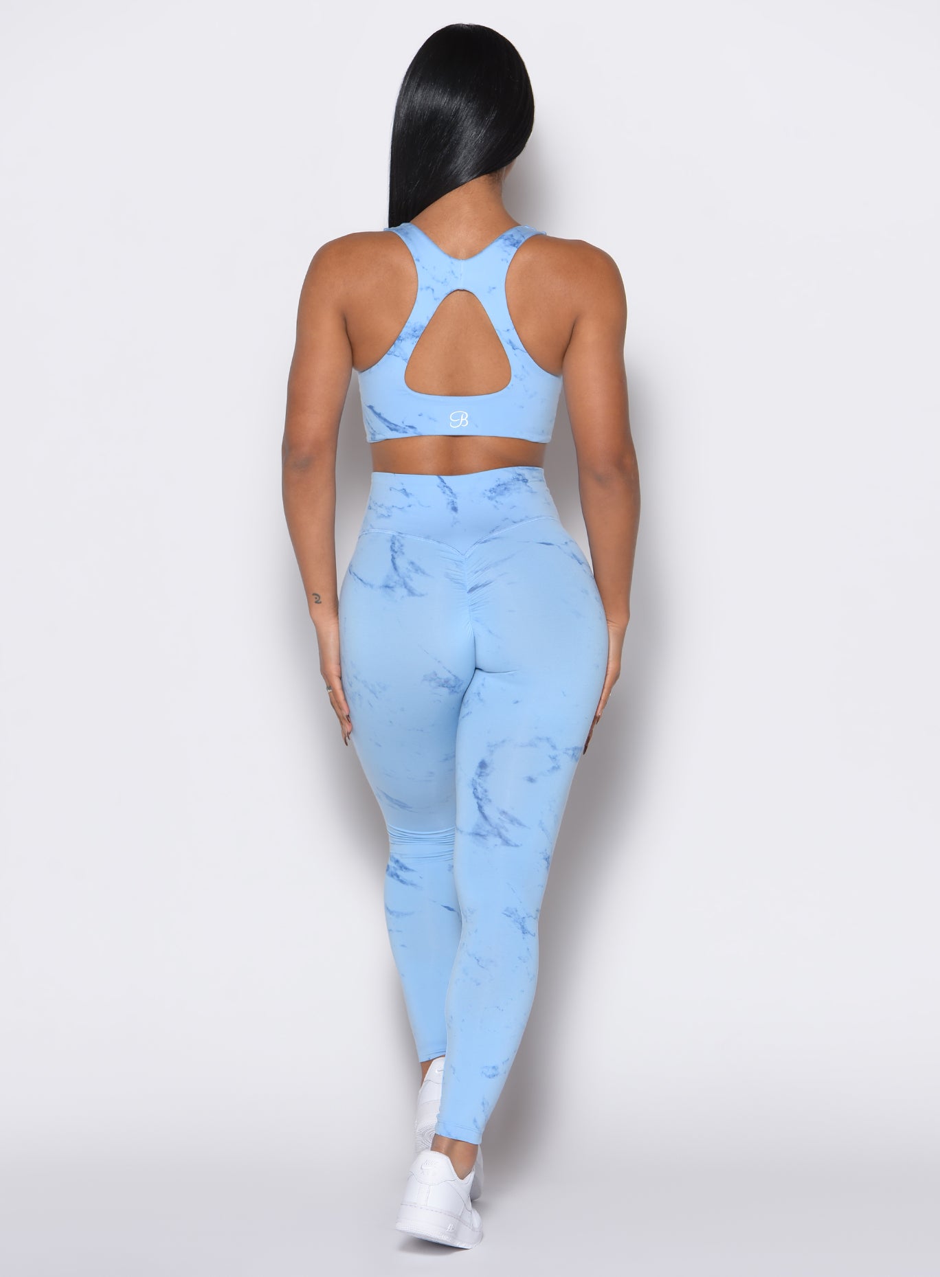 back profile view of a model wearing our fit marble leggings in Blue Jay color along with a matching bra