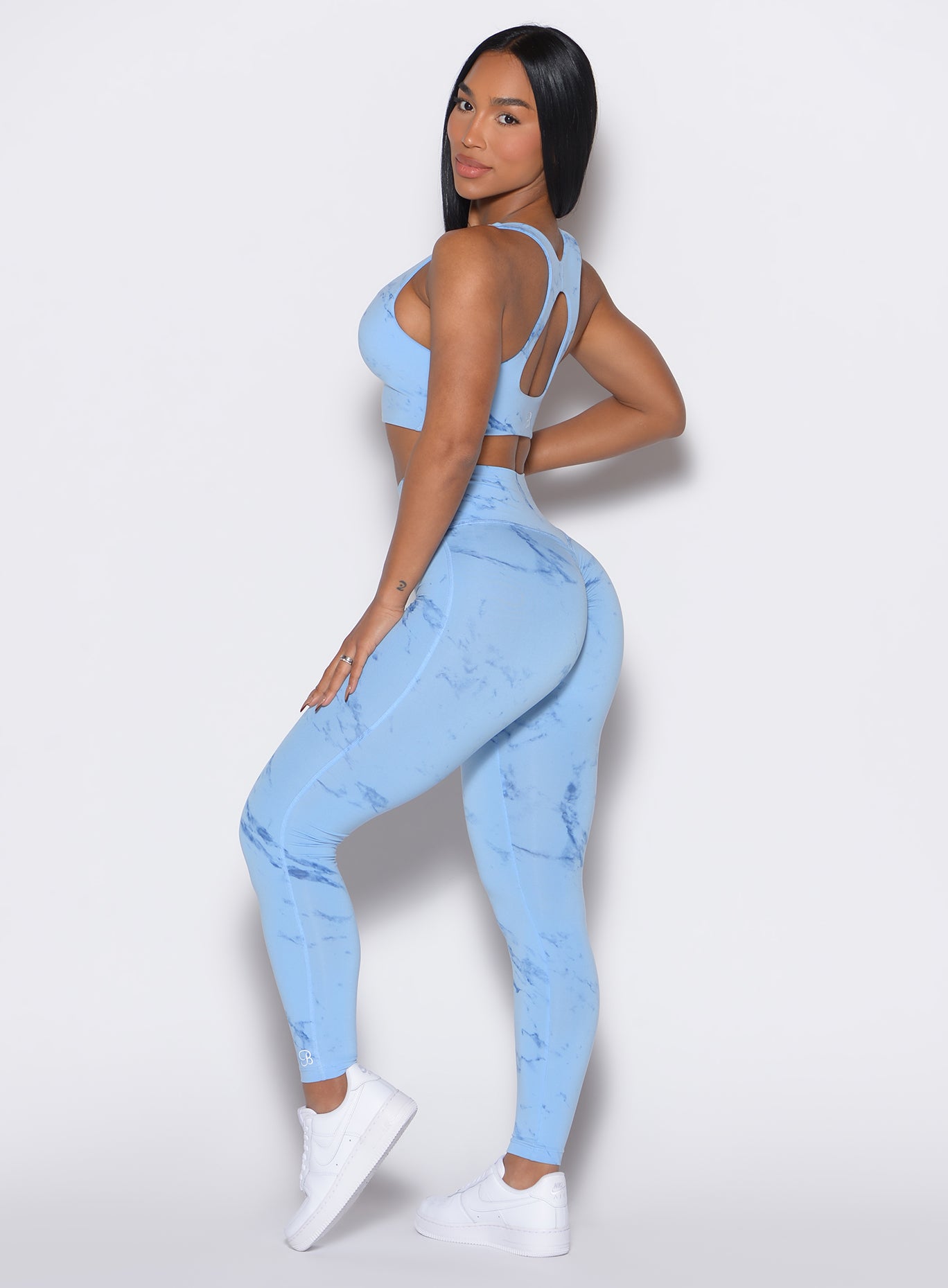 left side profile view of a model facing to her left wearing our fit marble leggings in Blue Jay color along with a matching bra