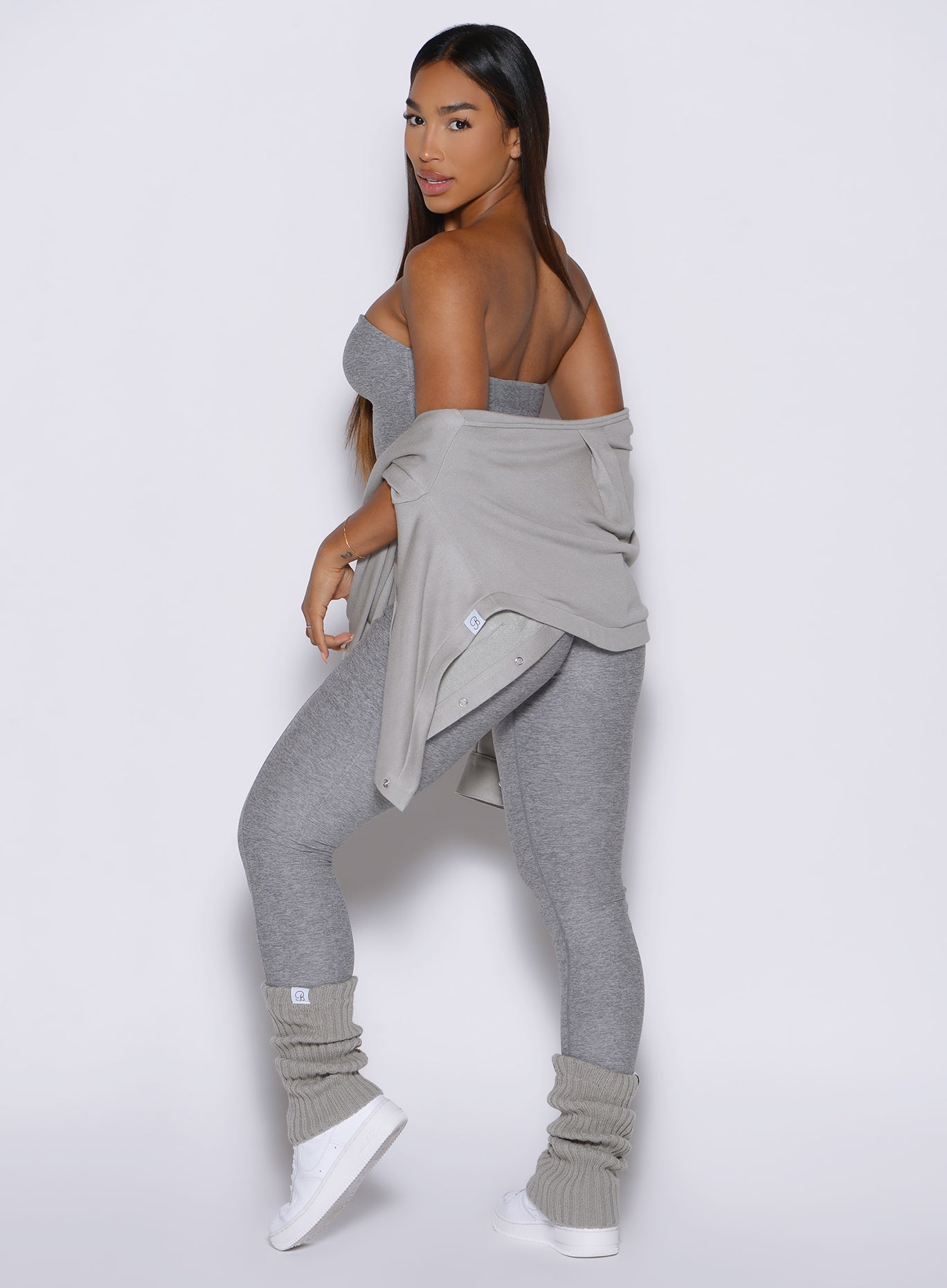 left side profile view of a model looking over her shoulder wearing the flawless form bodysuit and luxe leg warmers-short in dark and stormy color