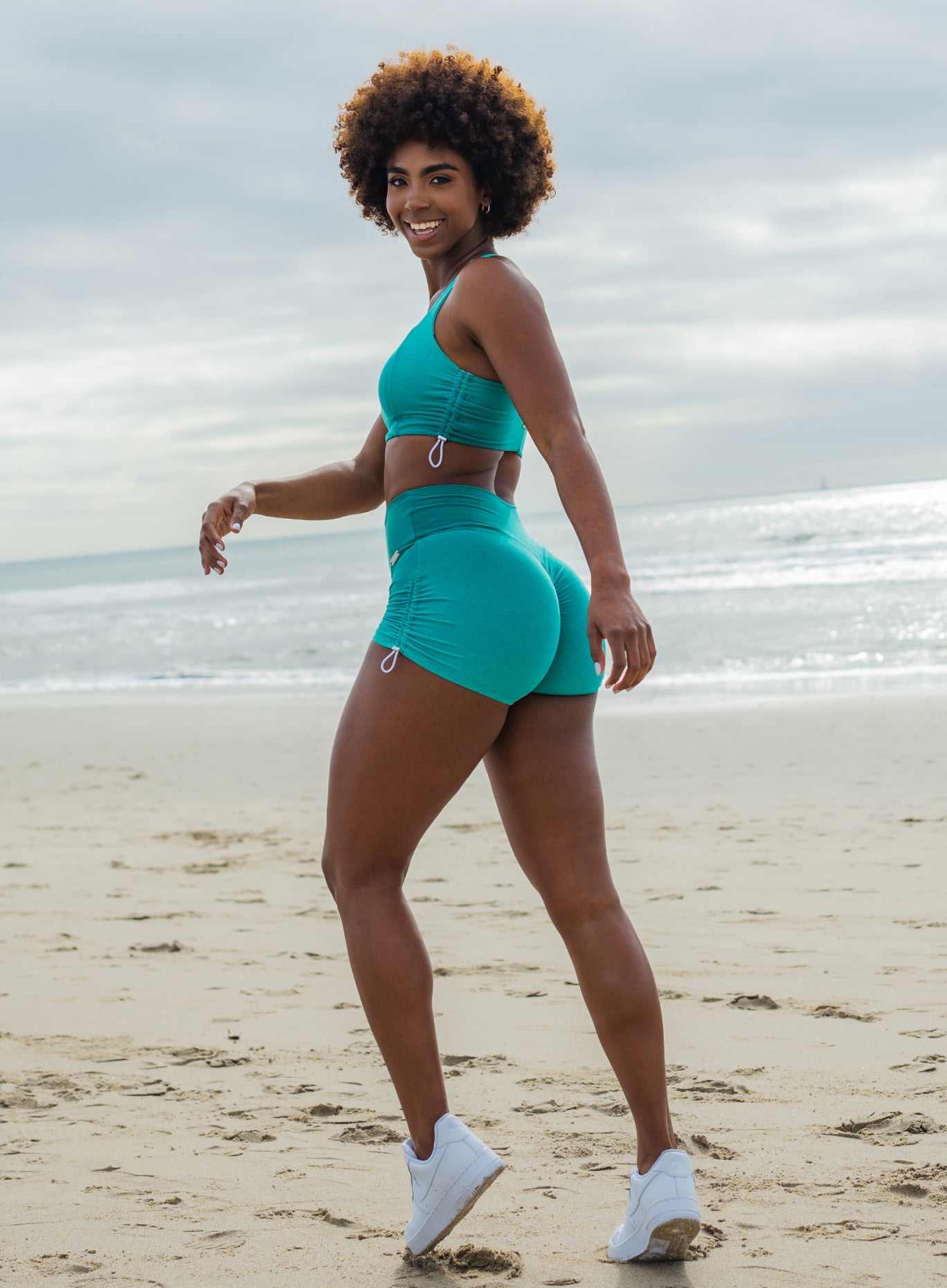 Woman in green athletic sports bra and matching shorts running on a beach