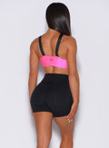 Back profile view of a model wearing our glow sports bra in neon pink and a pair of black shorts