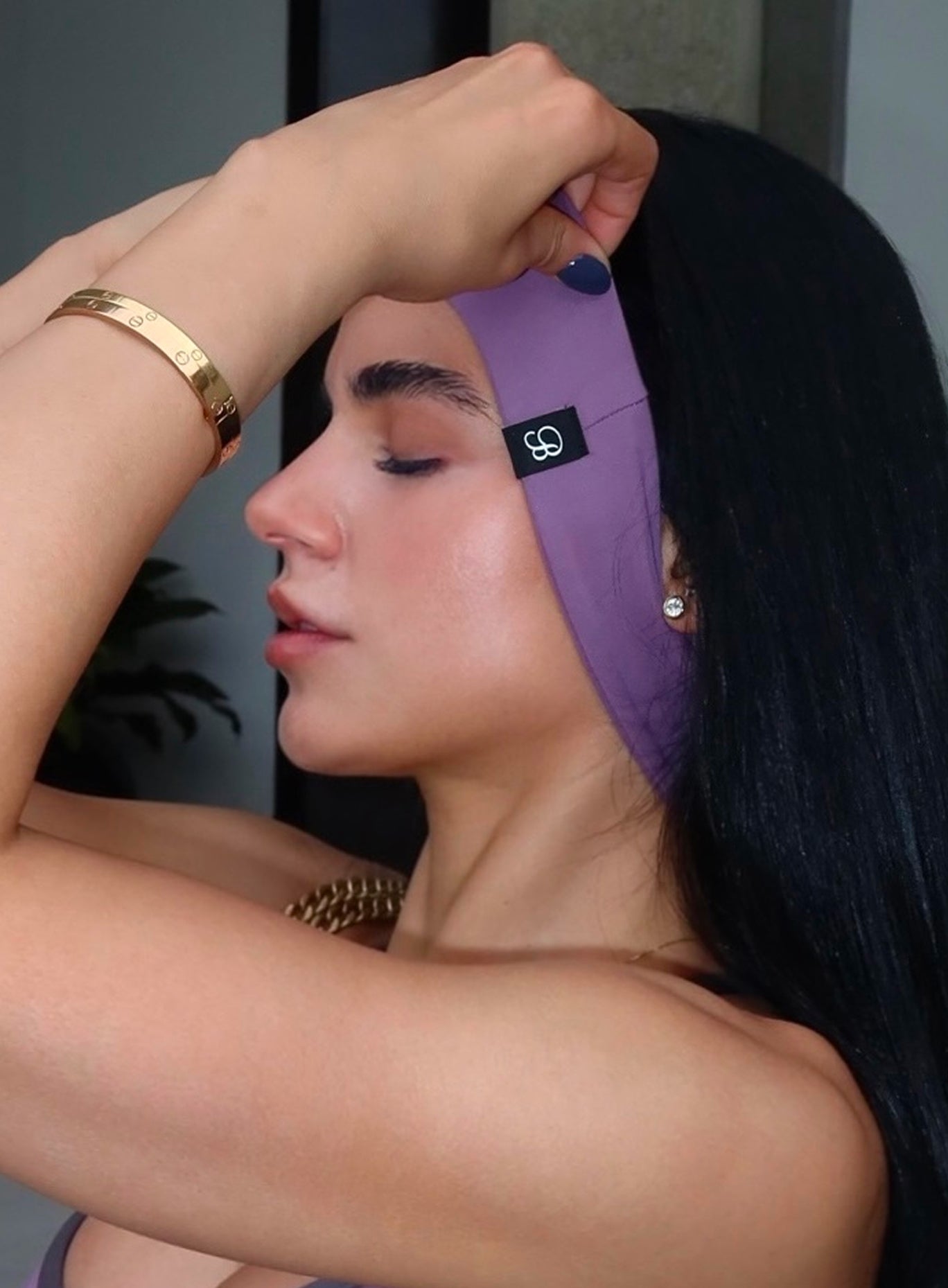 A woman wearing a wide, comfortable purple athletic headband with a small black logo patch, shown in profile with her arm raised.