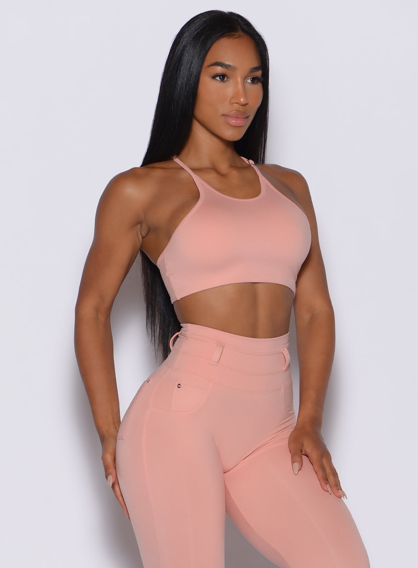 front profile view of a model angled slightly to her right wearing our high neck crop bra in pale blush color along with a matching leggings
