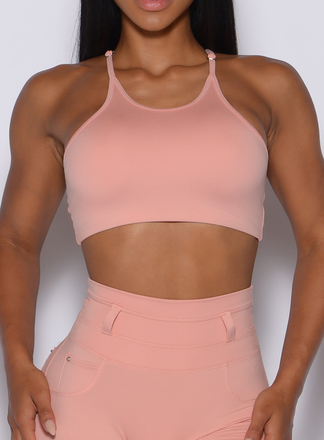 zoomed in front view of a model wearing our high neck crop bra in pale blush color along with the matching leggings