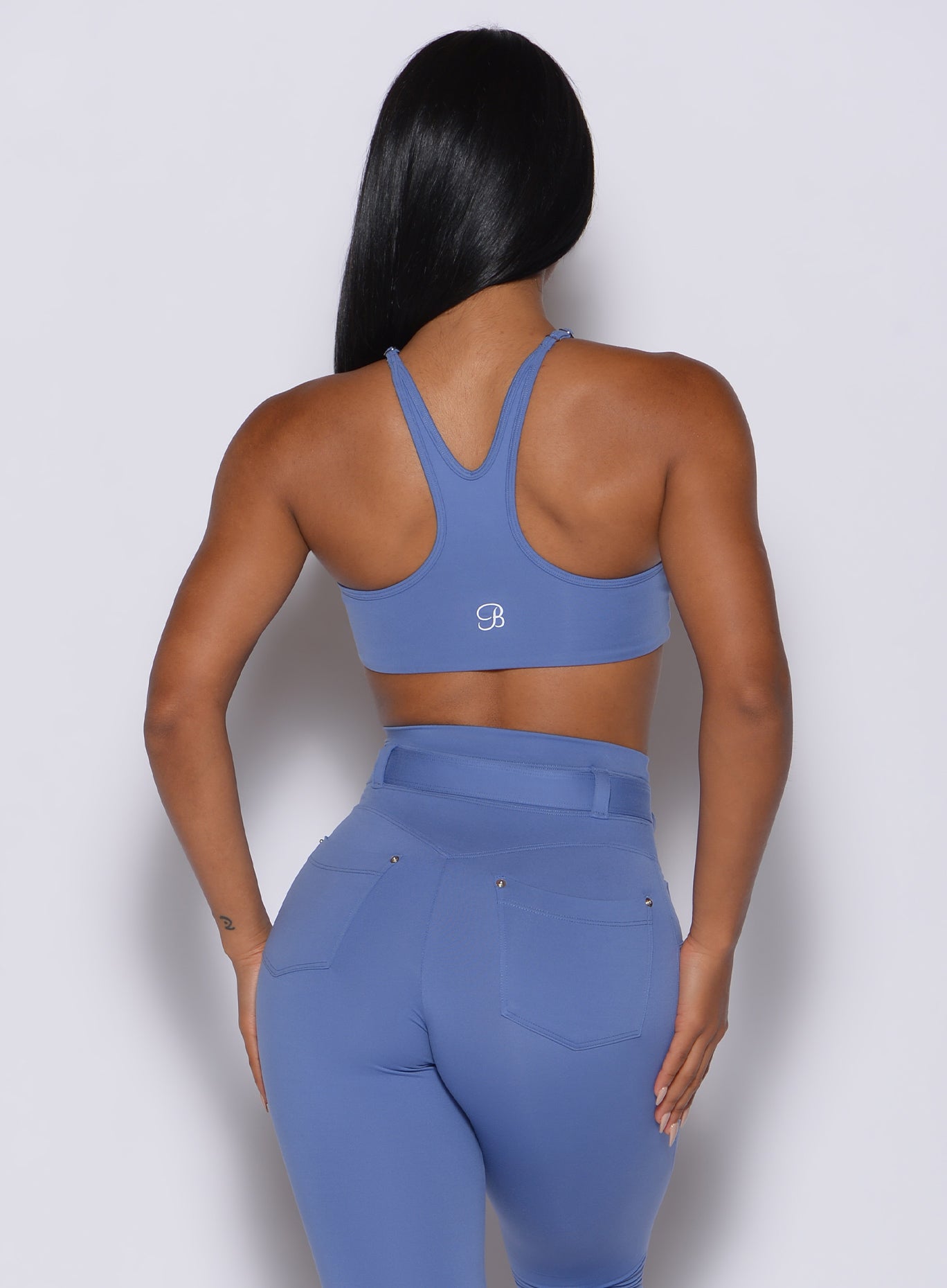 back profile view of a model wearing our high neck crop bra in denim blue color along with the matching leggings