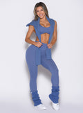front profile view of a model wearing the Luxe Leg Warmers in blue chill color   with the matching pullover draped over her shoulder