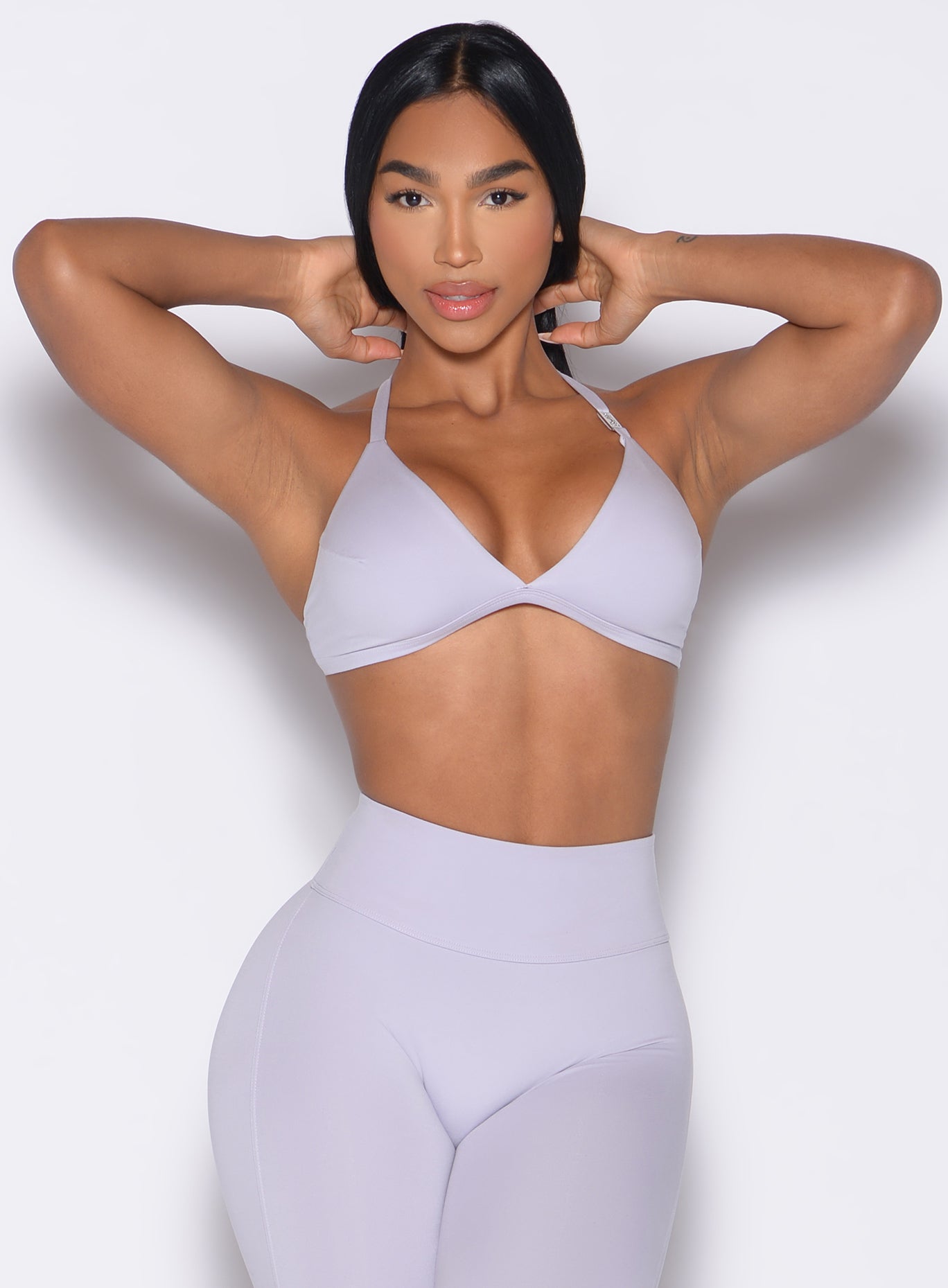 front profile view of a model in a hair tying pose wearing the Kini Bra in Galactic Lilac color