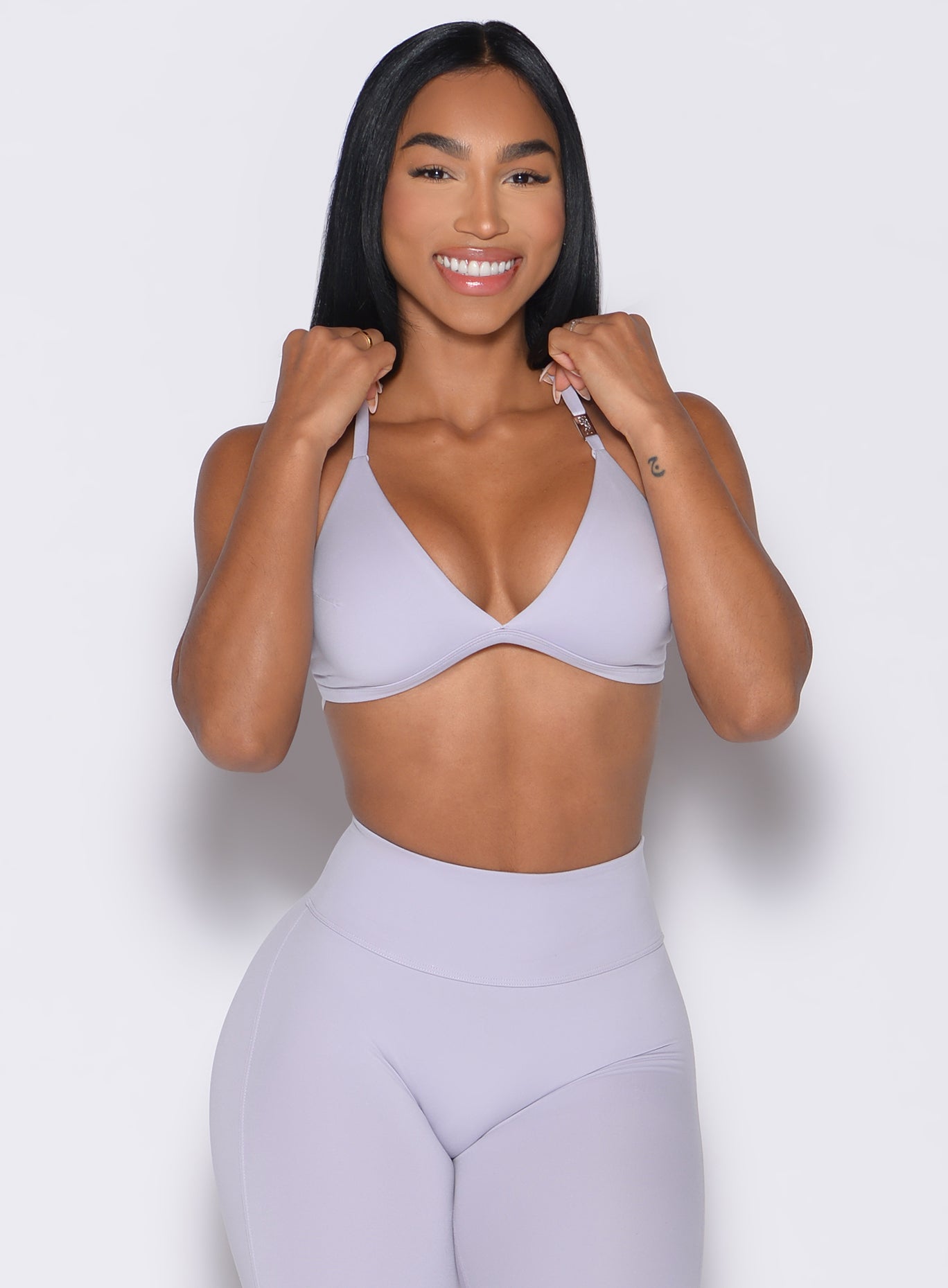 front profile view of a model with both hands on the straps of the bra wearing the Kini Bra in Galactic Lilac color