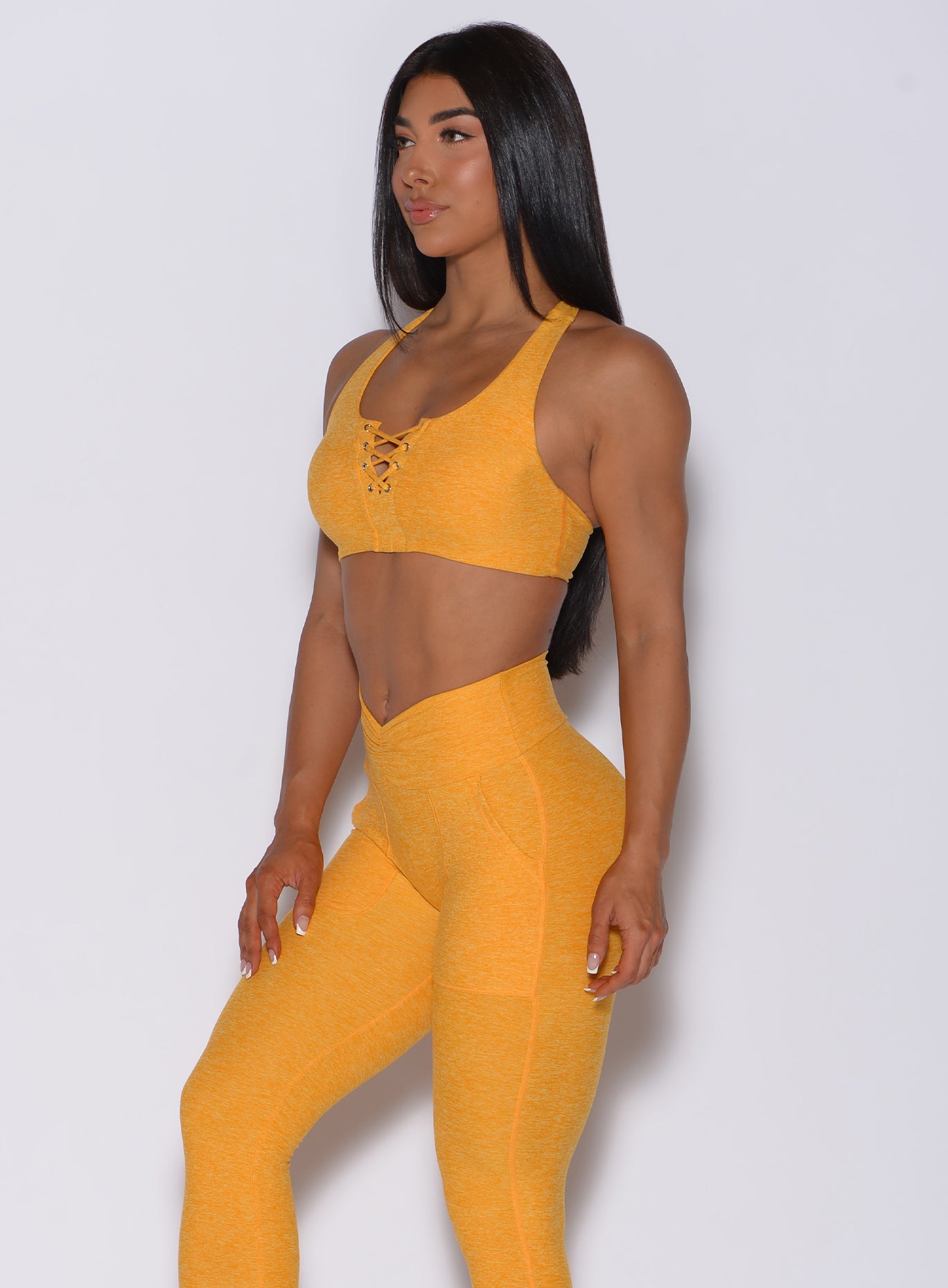Left side profile view of a model angled to her left wearing our laced crop bra in sunkissed color and a matching leggings