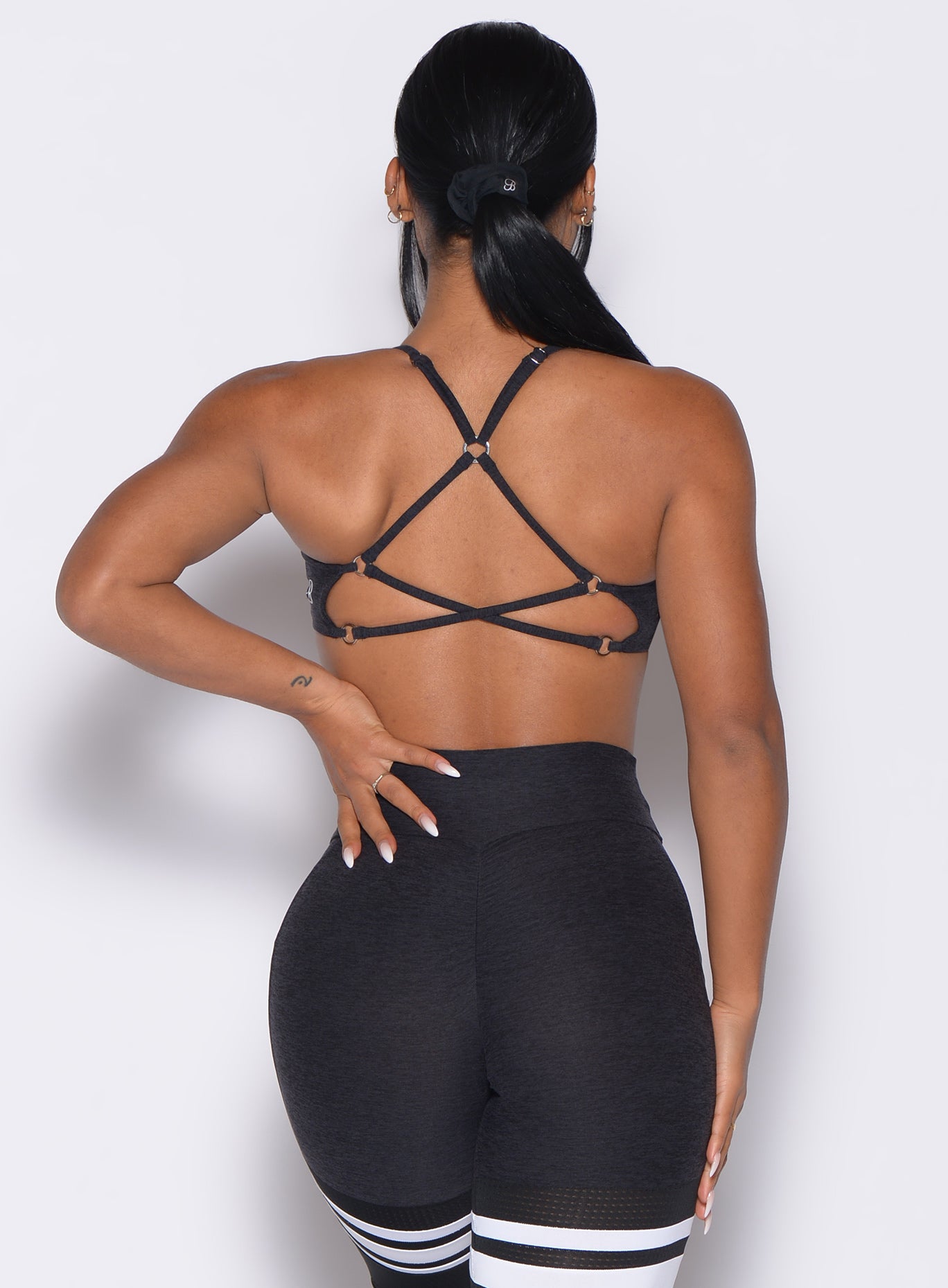 back profile view of a model with one hand on her waist wearing the Lift Luxe Sports bra in Heathered black color