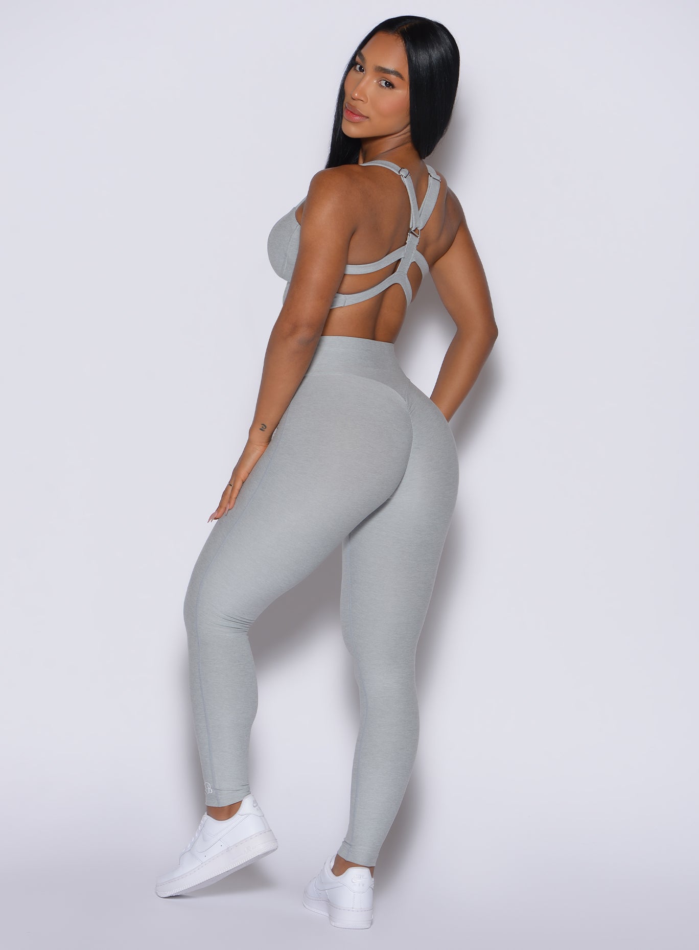 back profile of model facing to her left wearing the Movement Leggings in Light Cloud color and a matching Sports Bra