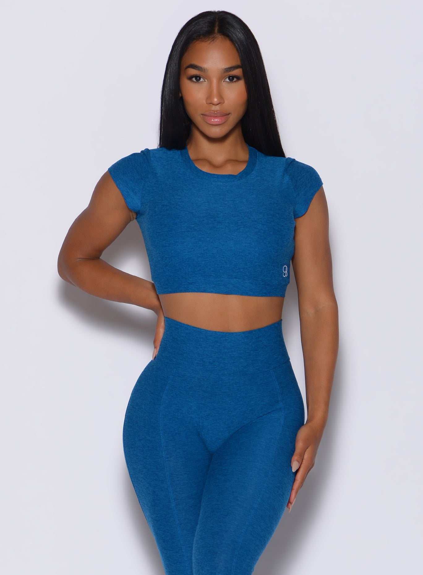 Front profile view of a model facing forward wearing our open back tee in azure color and a matching high rise leggings