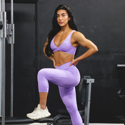 Woman in purple athletic bra and capri leggings stretching in a gym setting