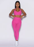 front profile view of a model adjusting her waistband wearing our V back leggings in Neon pink sorbet color along with a matching bra