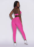 back profile view of a model wearing our V back leggings in Neon pink sorbet color along with a matching bra