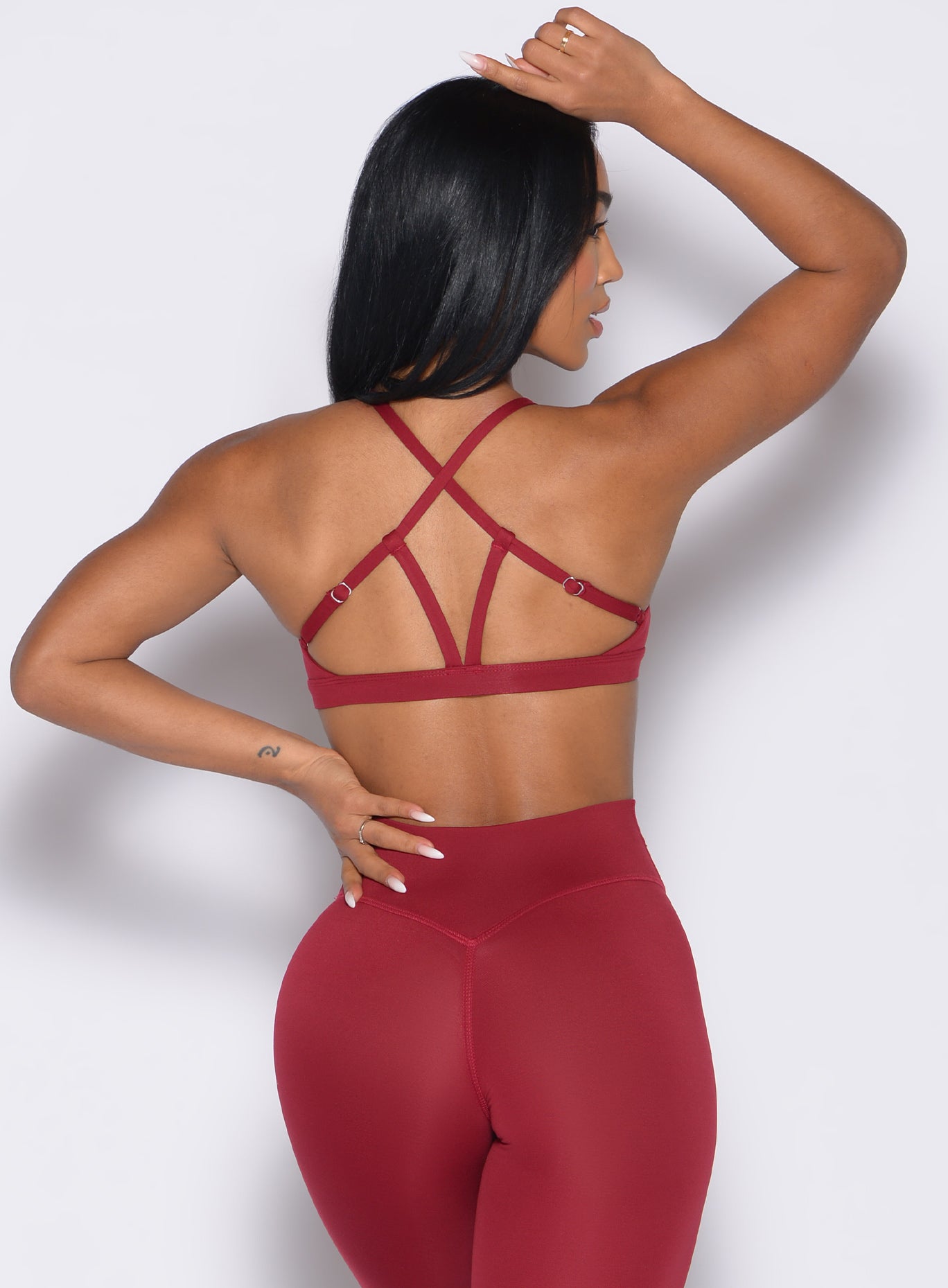 back profile view of a model with one hand on her waist wearing the Passion Sports Bra in red velvet color
