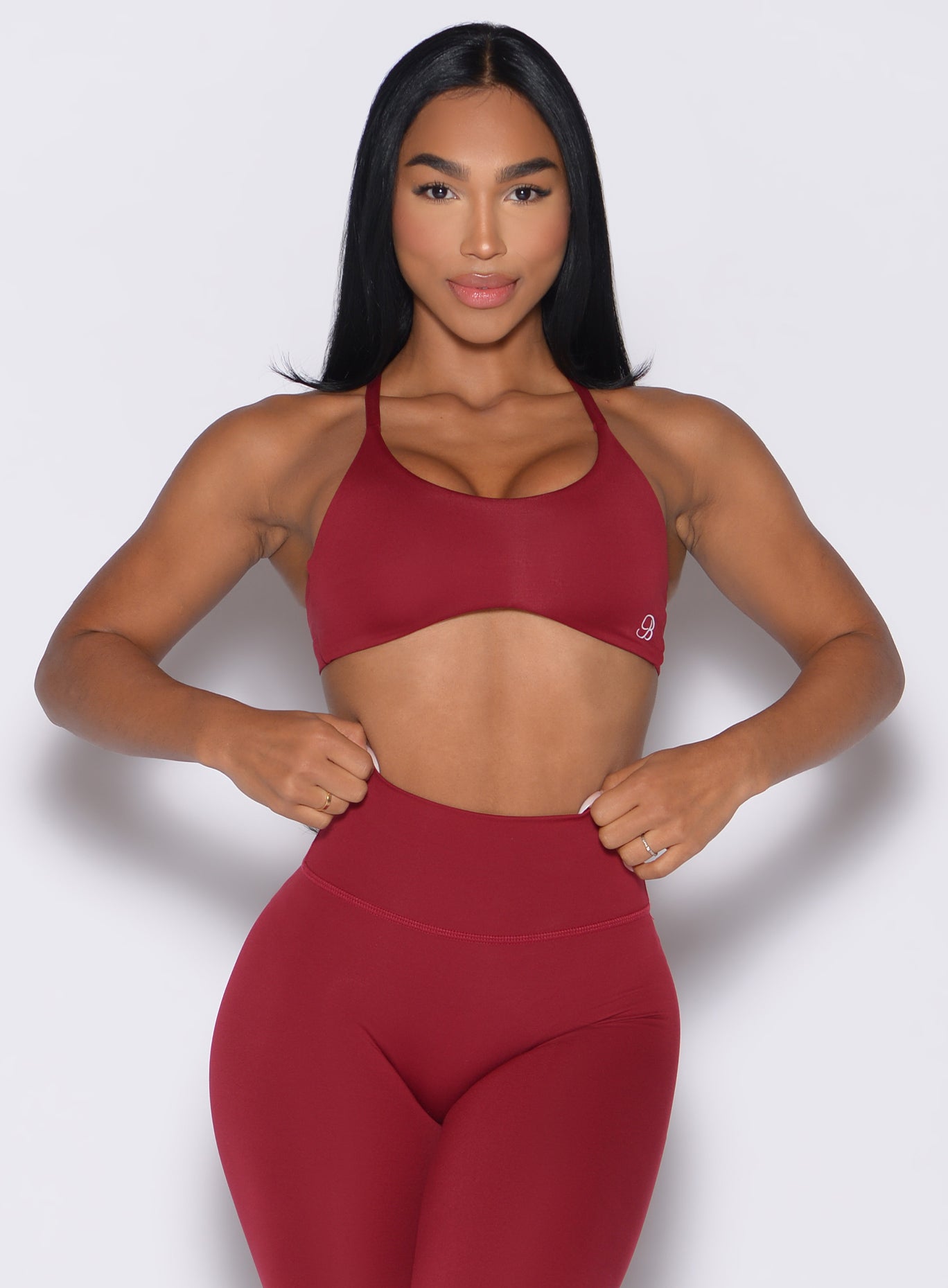 front profile view of a model adjusting the waistband of the leggings wearing the Passion Sports Bra in red velvet color