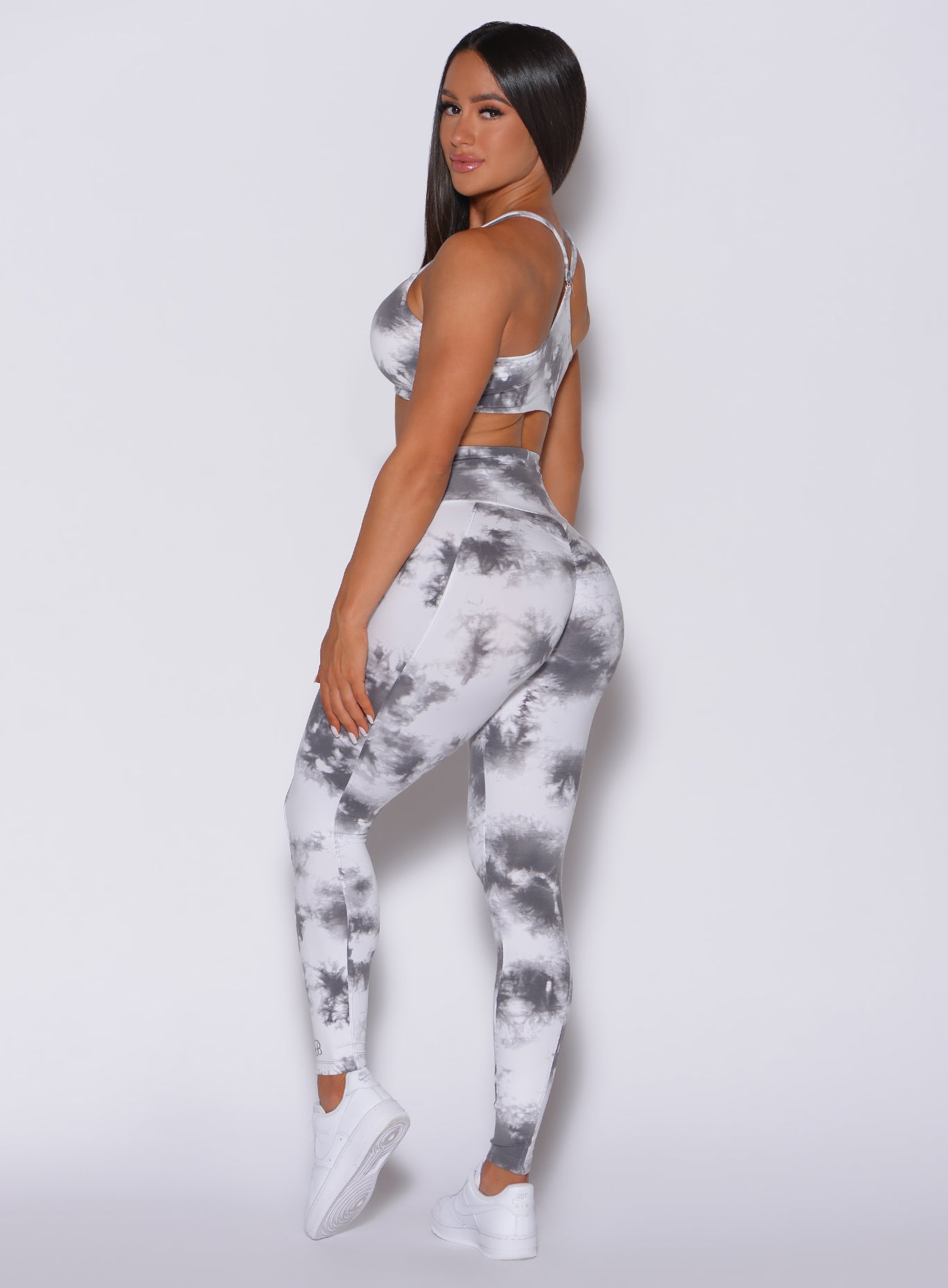Left side profile picture of a model facing to her left wearing our tie dye peach booty leggings in gray white along with a matching bra