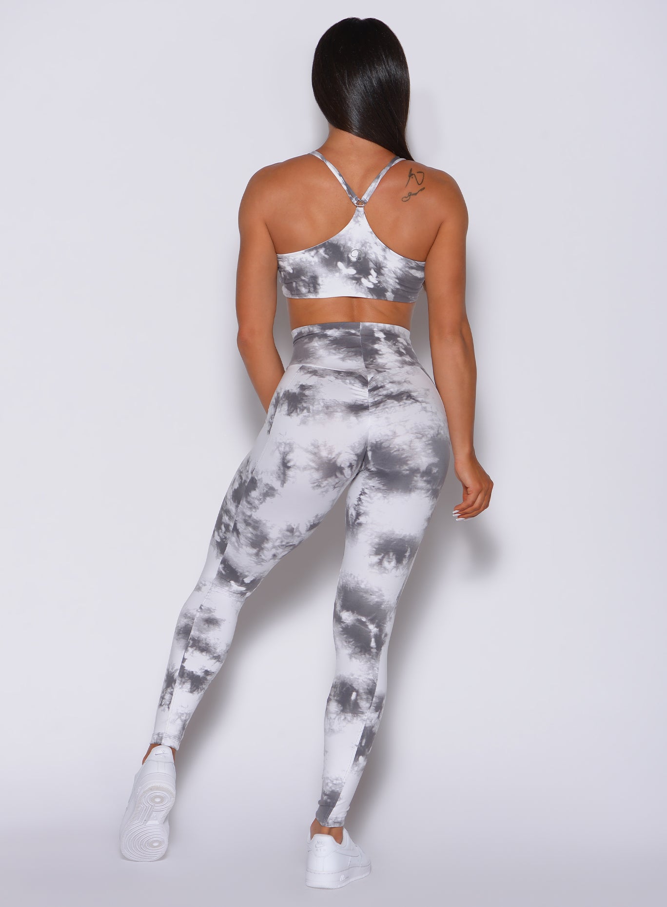 Back side profile view of a model in our tie dye peach booty leggings in gray white and a matching sports bra