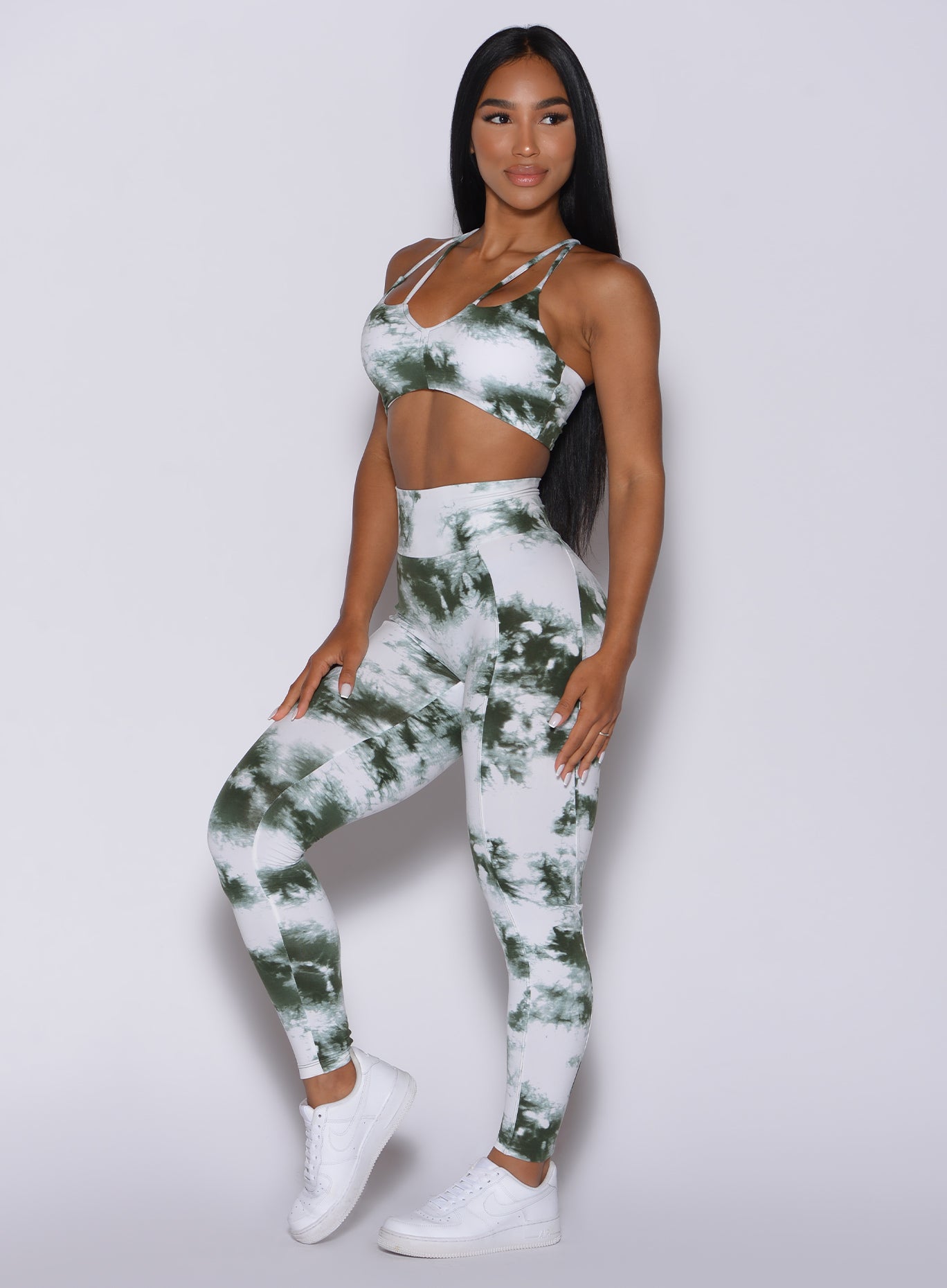 Left side profile view of a model angled to her left wearing our tie dye peach booty leggings in green white and a matching bra