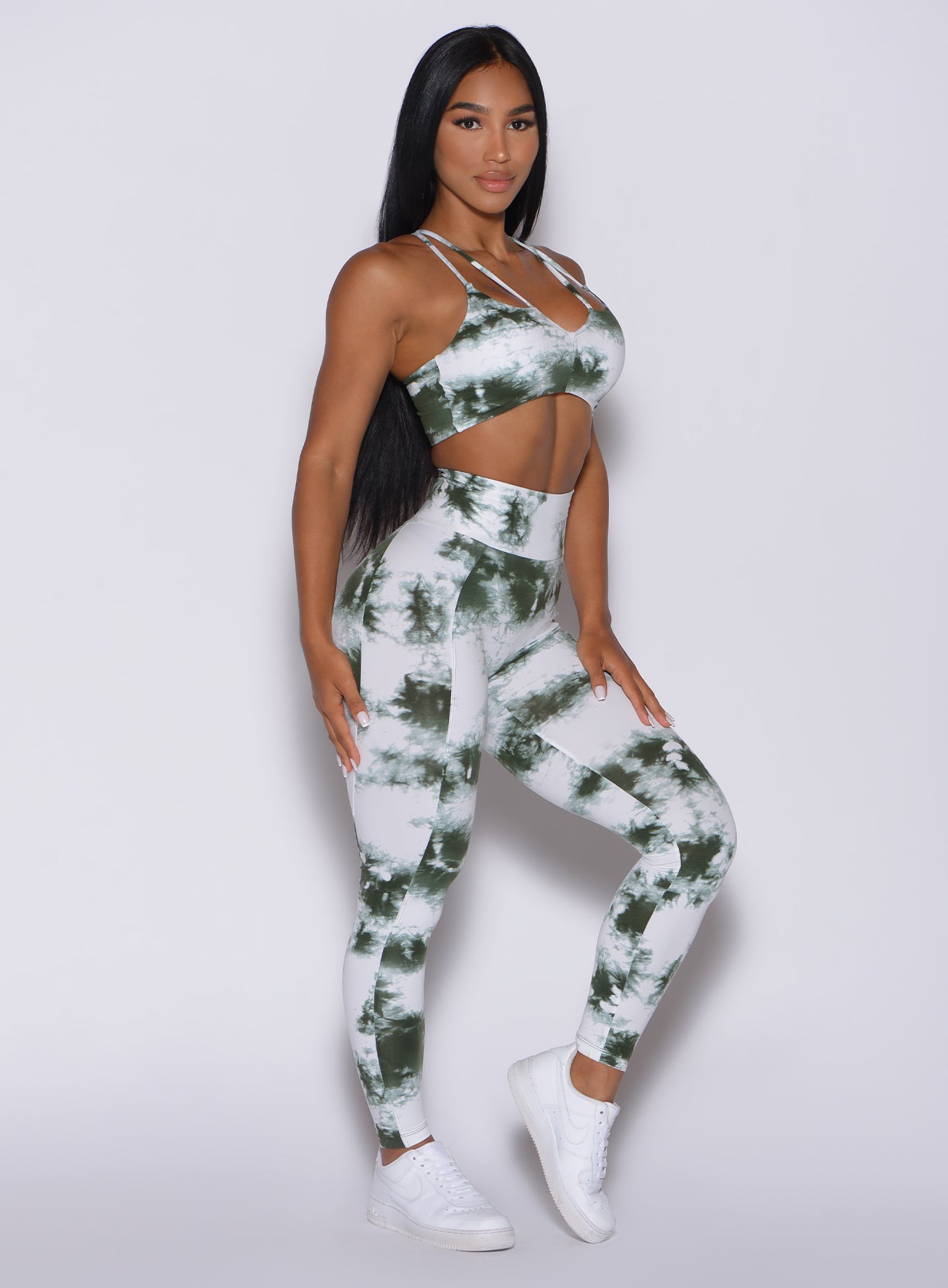 Right side profile view of a model angled to her right wearing our tie dye peach booty leggings in green white and a matching bra