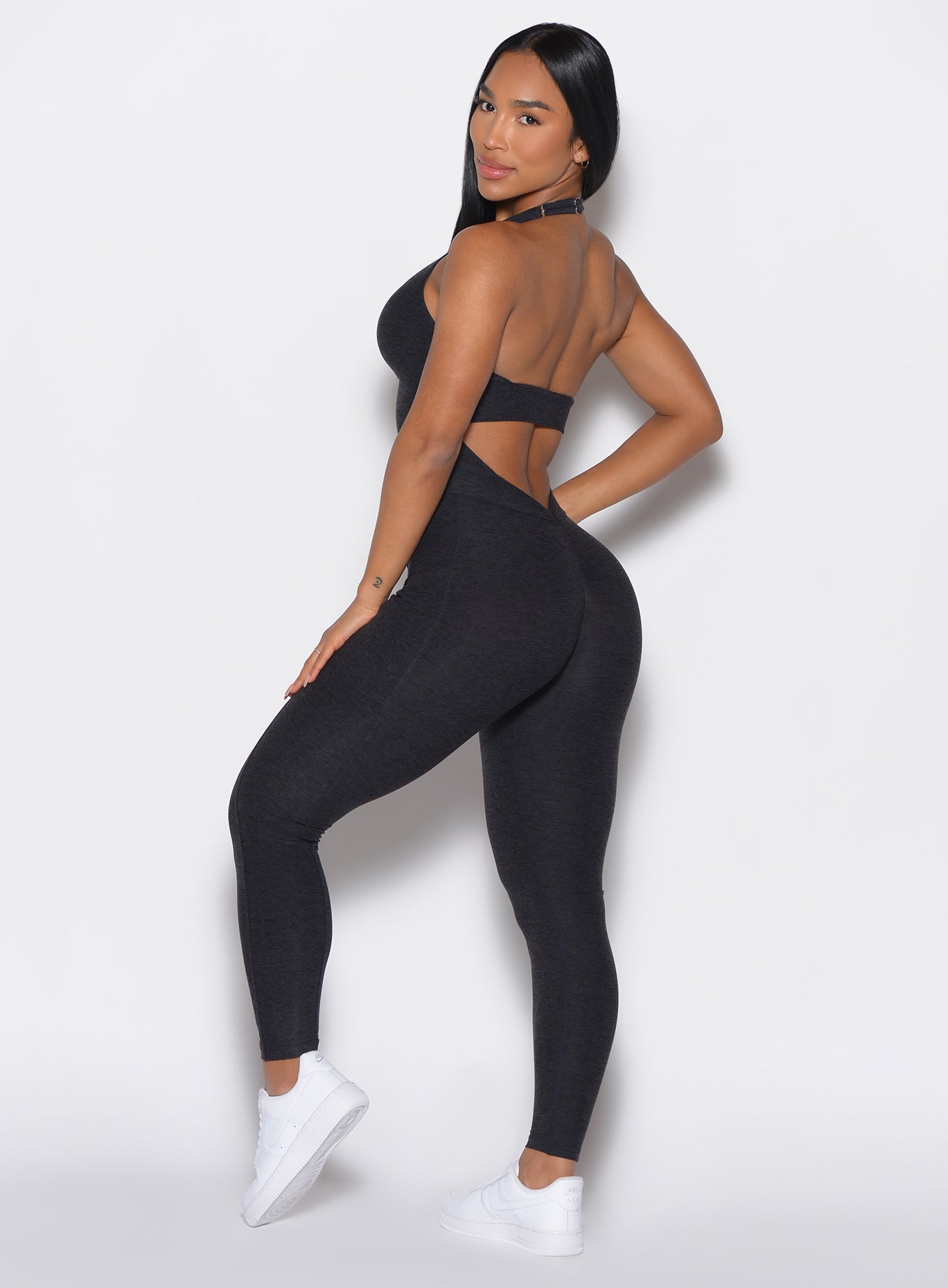 left profile view of a model facing to her left wearing our Backless Pocket Bodysuit in onyx black
