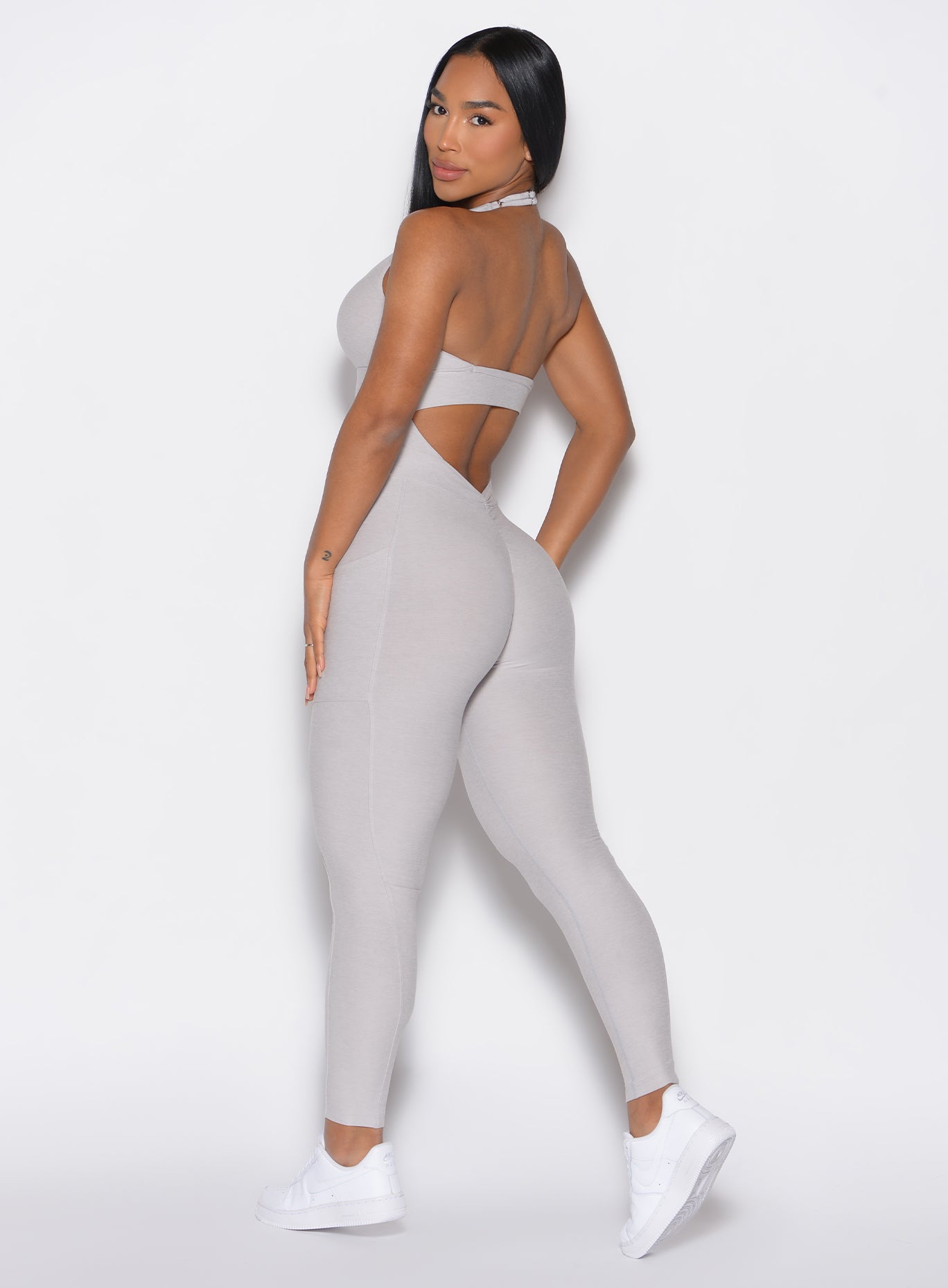 left side profile view of a model facing to her left wearing our Backless Pocket Bodysuit in ice color