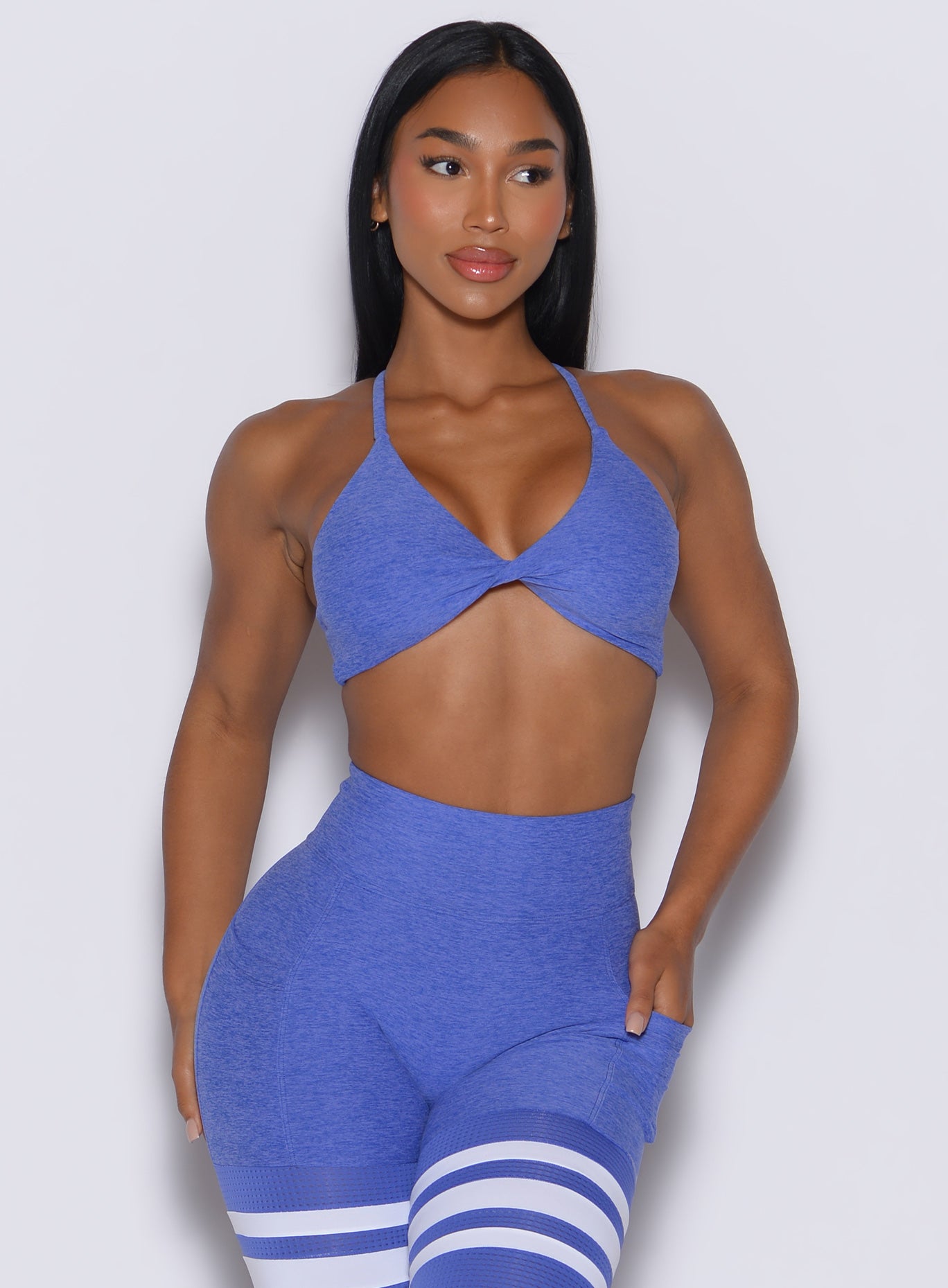 A front profile view of a model facing forward while wearing our twist mini bra in violet blue, paired with matching thigh-high leggings.