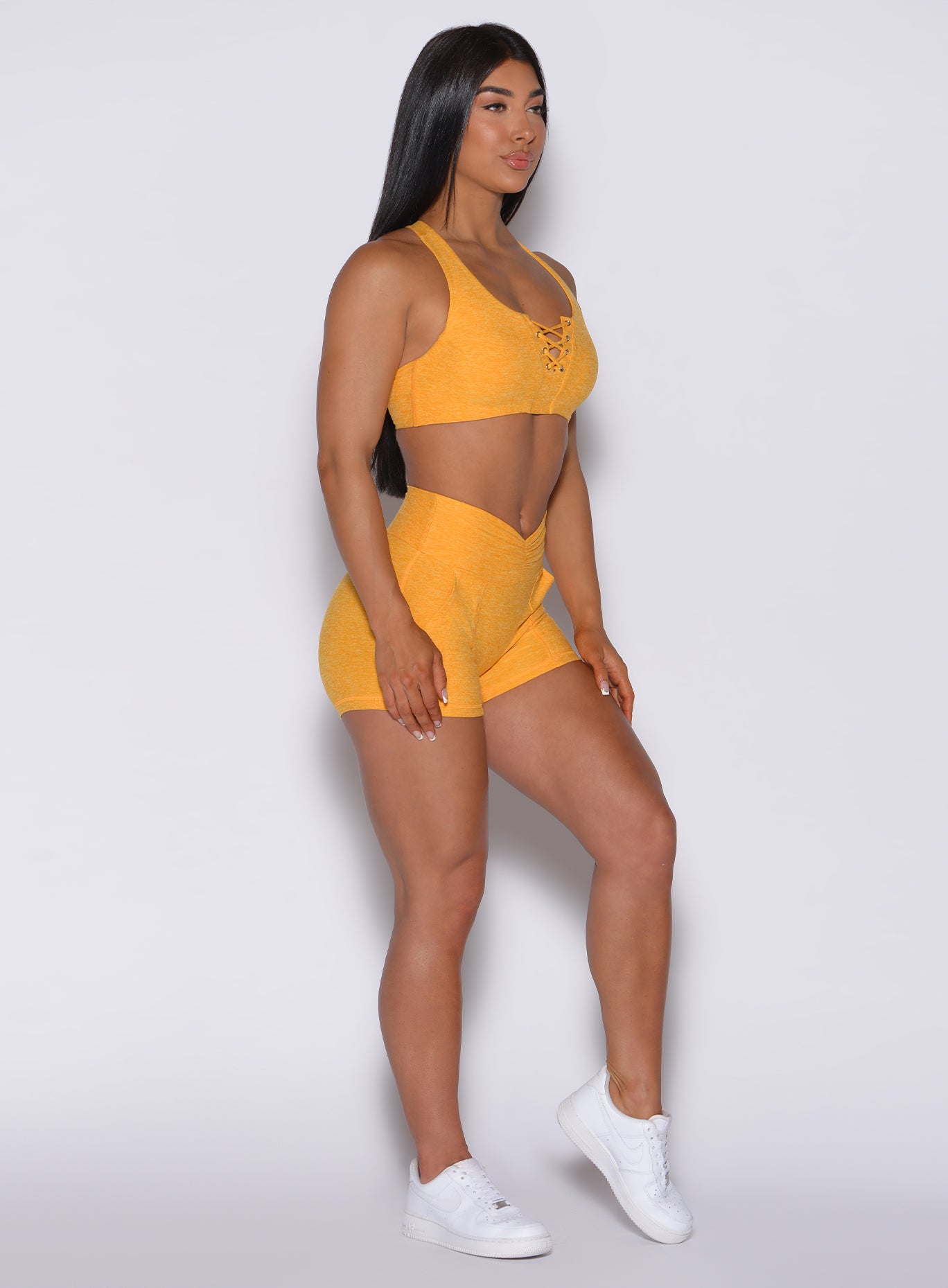 Right side profile view of a model facing forward wearing our V scrunch shorts in sunkissed color and a matching bra