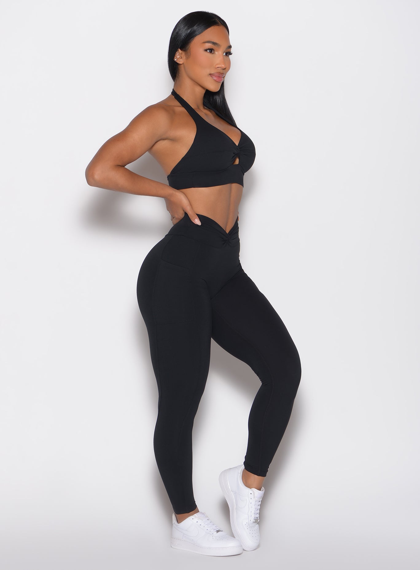 right side profile view of a model with one hand on her waist wearing the Sculpt Knot Leggings in black color